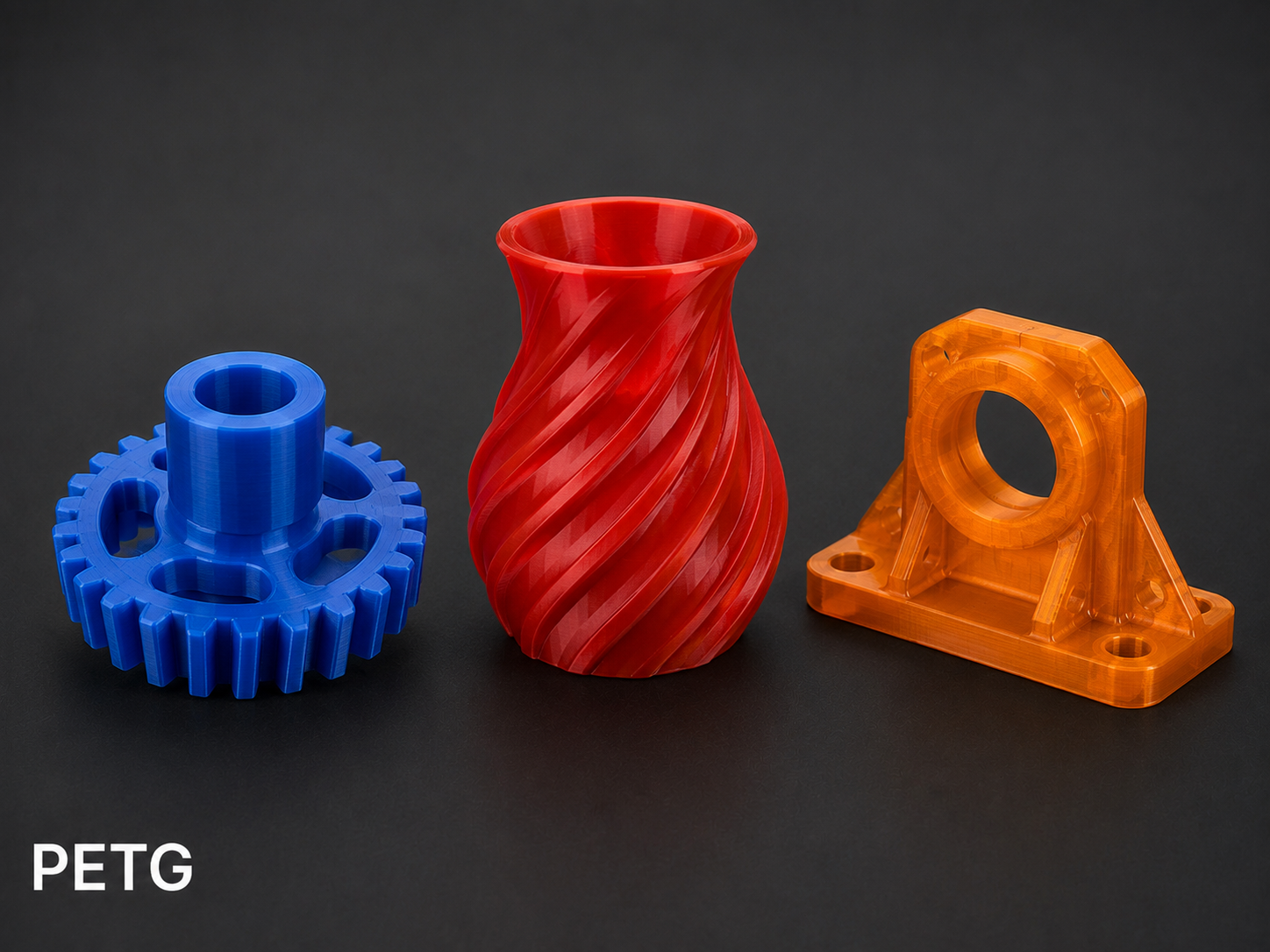 Three colorful 3D-printed objects in black background: blue gear with a cylindrical extension, red twisted vase, and orange pulley with a base.