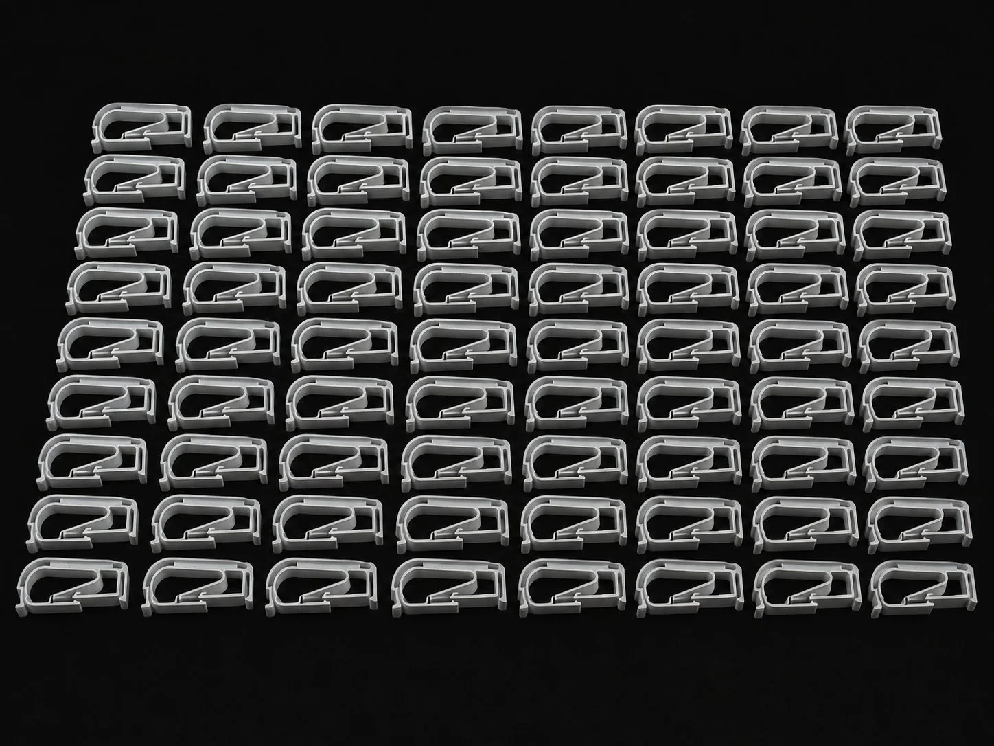 A grid of identical white plastic hooks arranged neatly on a black background.