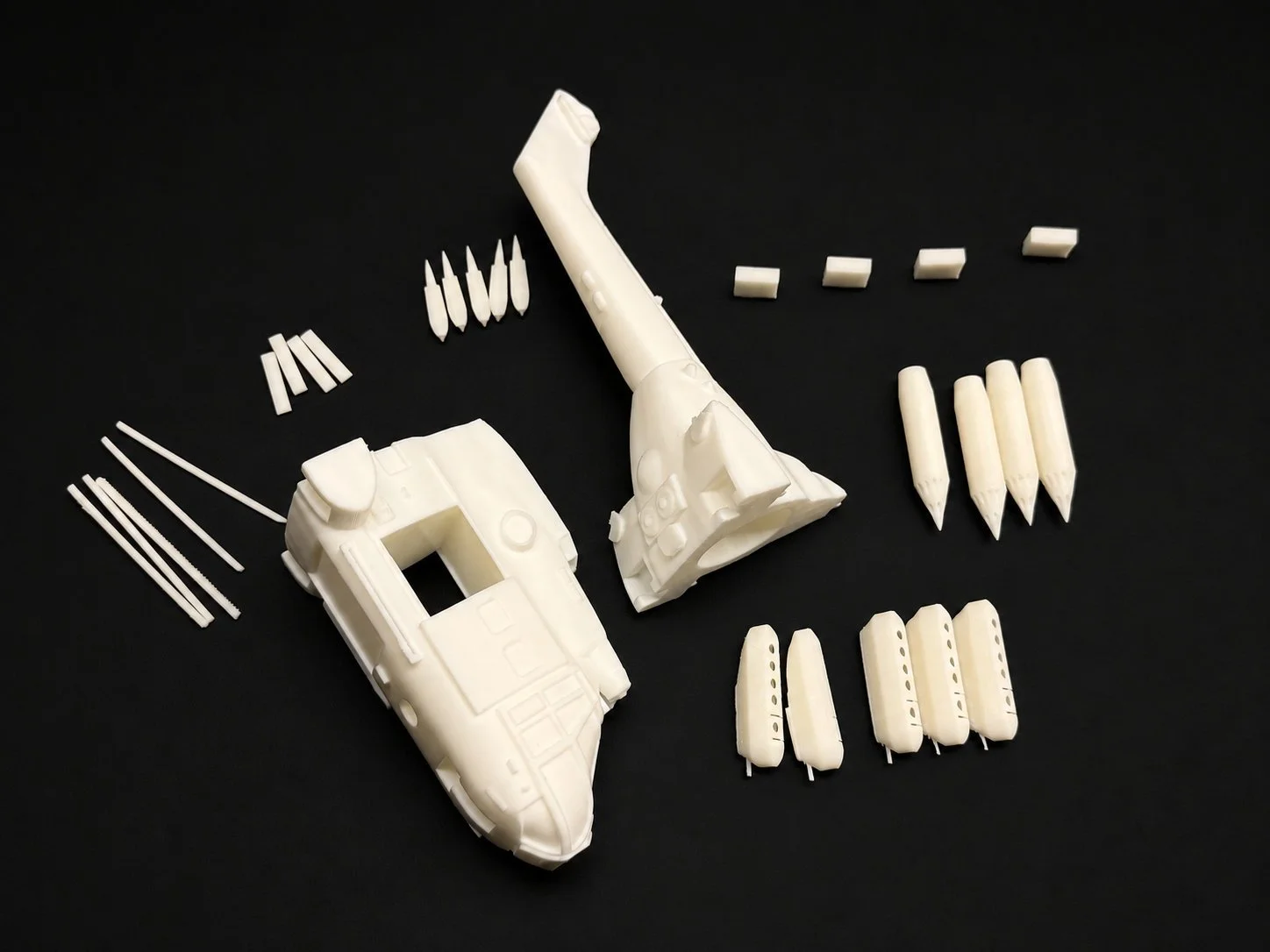 Disassembled white plastic model of a military helicopter with various parts and tools arranged on a black background