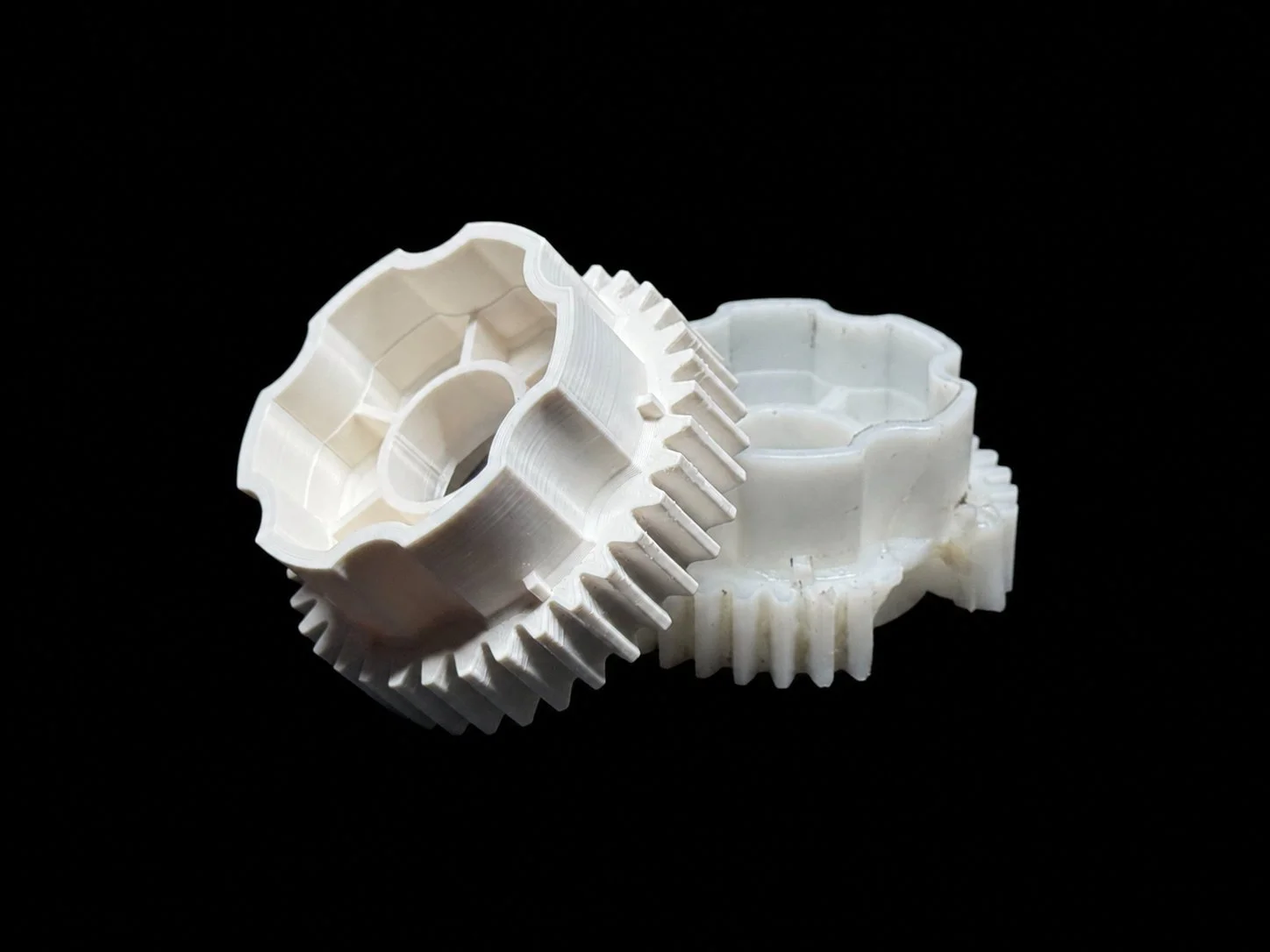 Two white plastic gears with teeth, placed on a black background.