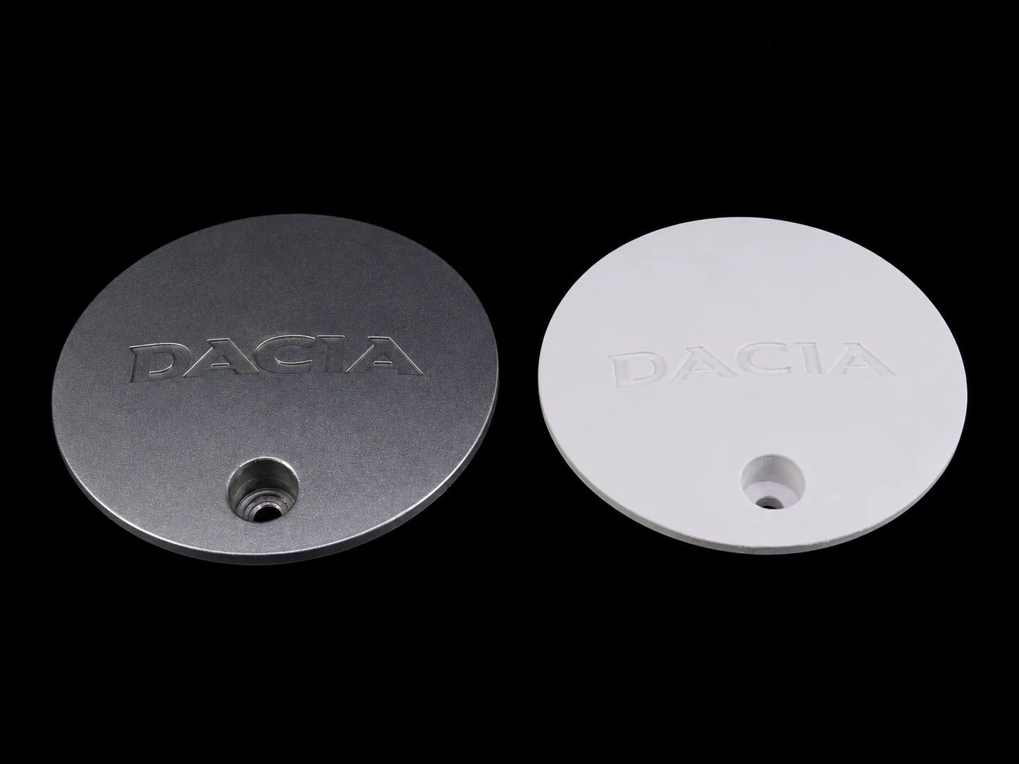 Two circular metal and plastic objects with the embossed word 'DACIA', each with a central hole, placed against a black background.