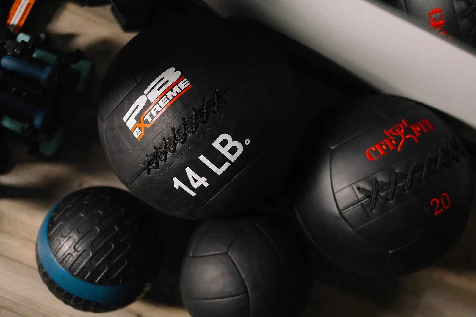 Several black medicine balls, one with the logo 'PEEXtreme' and the text '14 LB', another with red text 'CHICAGO 20', and a smaller black ball, arranged on a wooden floor implying that fitness is good for men in a sober house