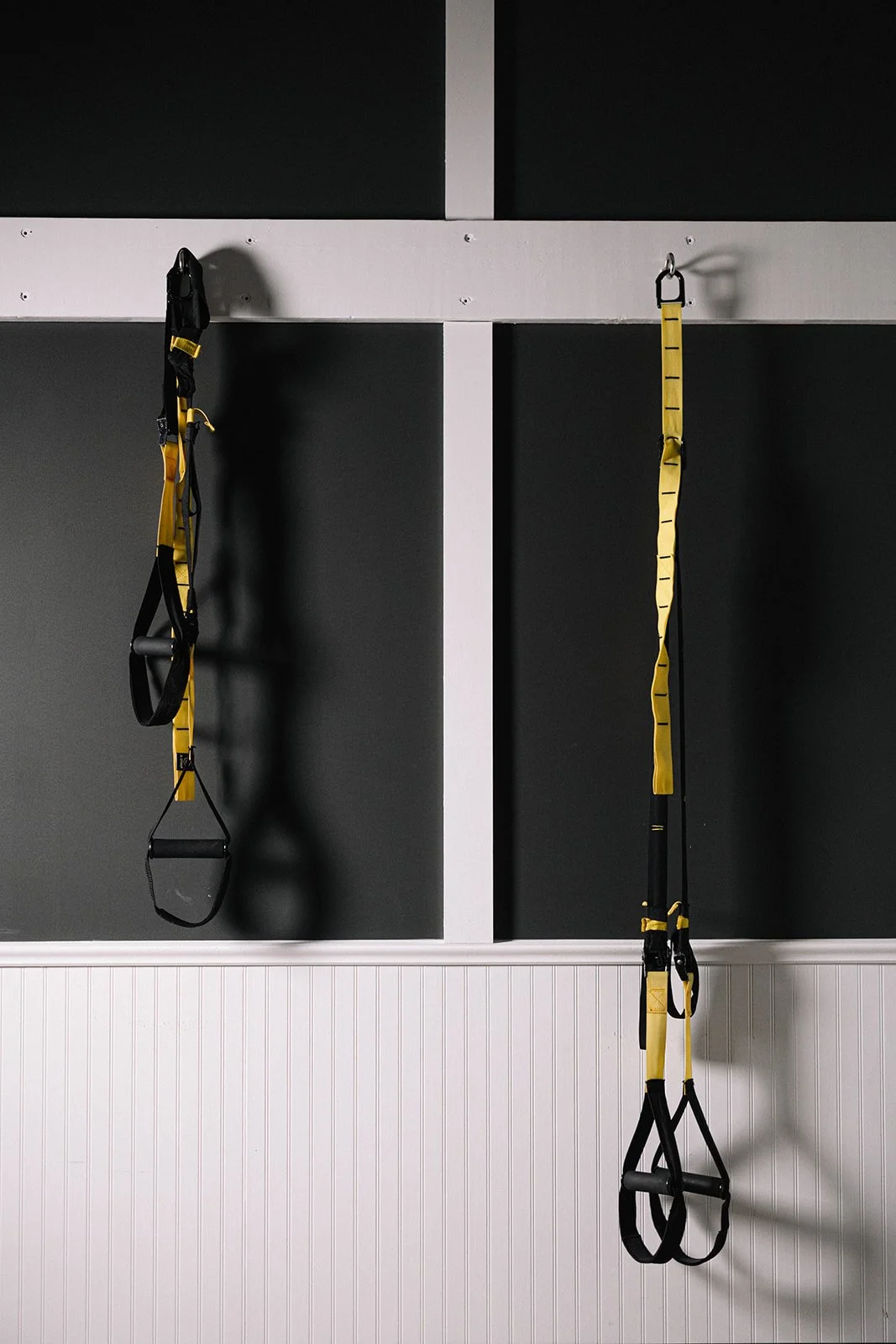 Two yellow and black TRX suspension training straps hanging on wall hooks in a gym.