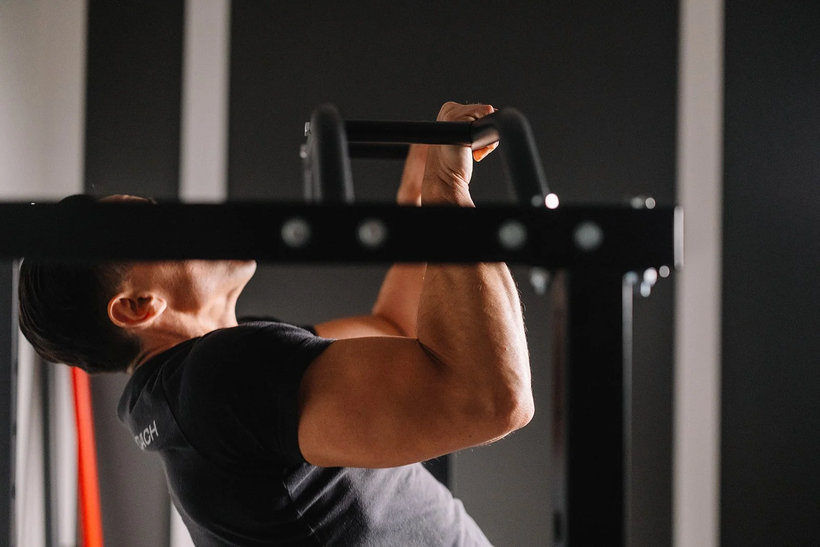 A sober person performing a pull-up exercise on a pull-up bar in a gym, with focus on their muscular arms and back.