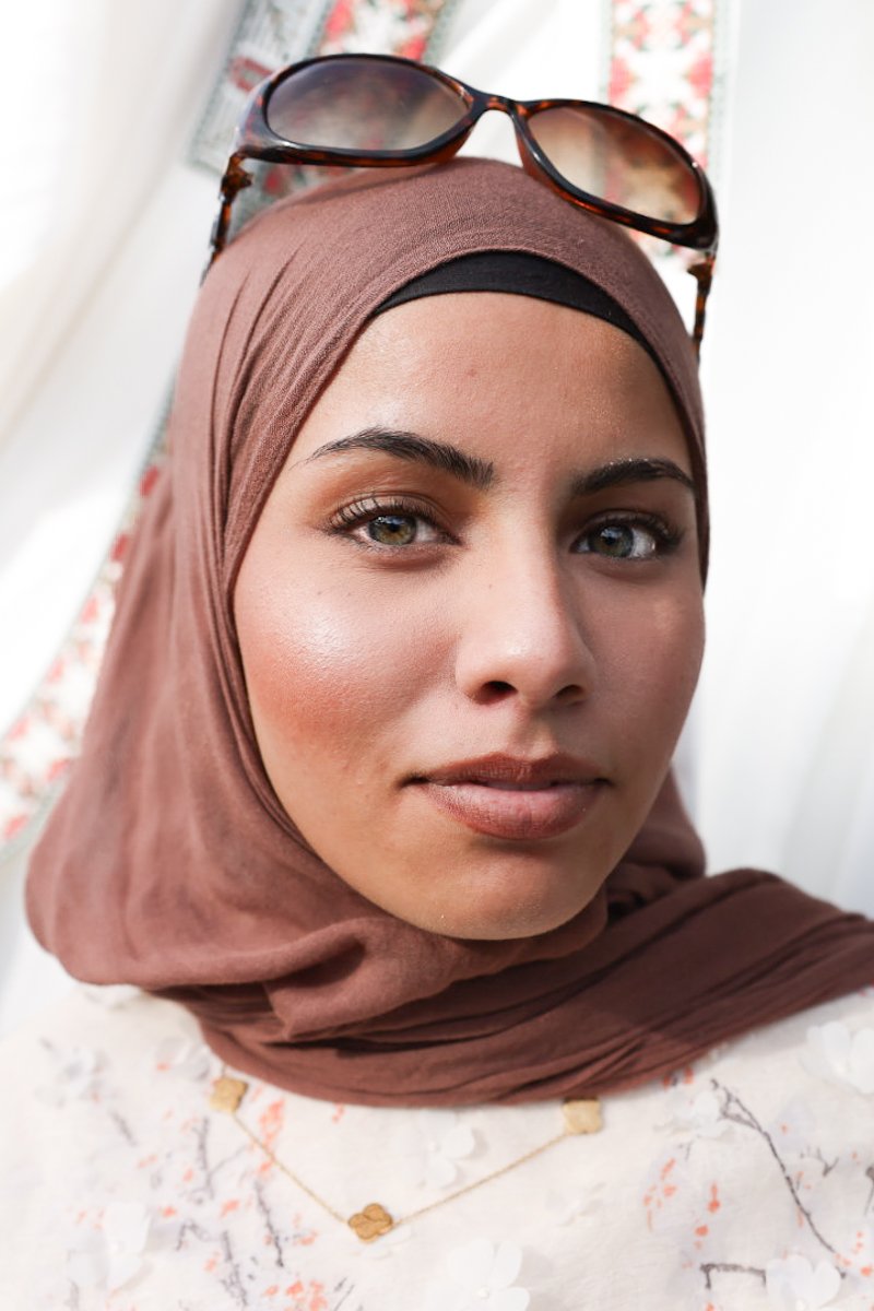 A close-up portrait of a woman in a brown headscarf with sunglasses resting on top at the Carmel Eid Festival.