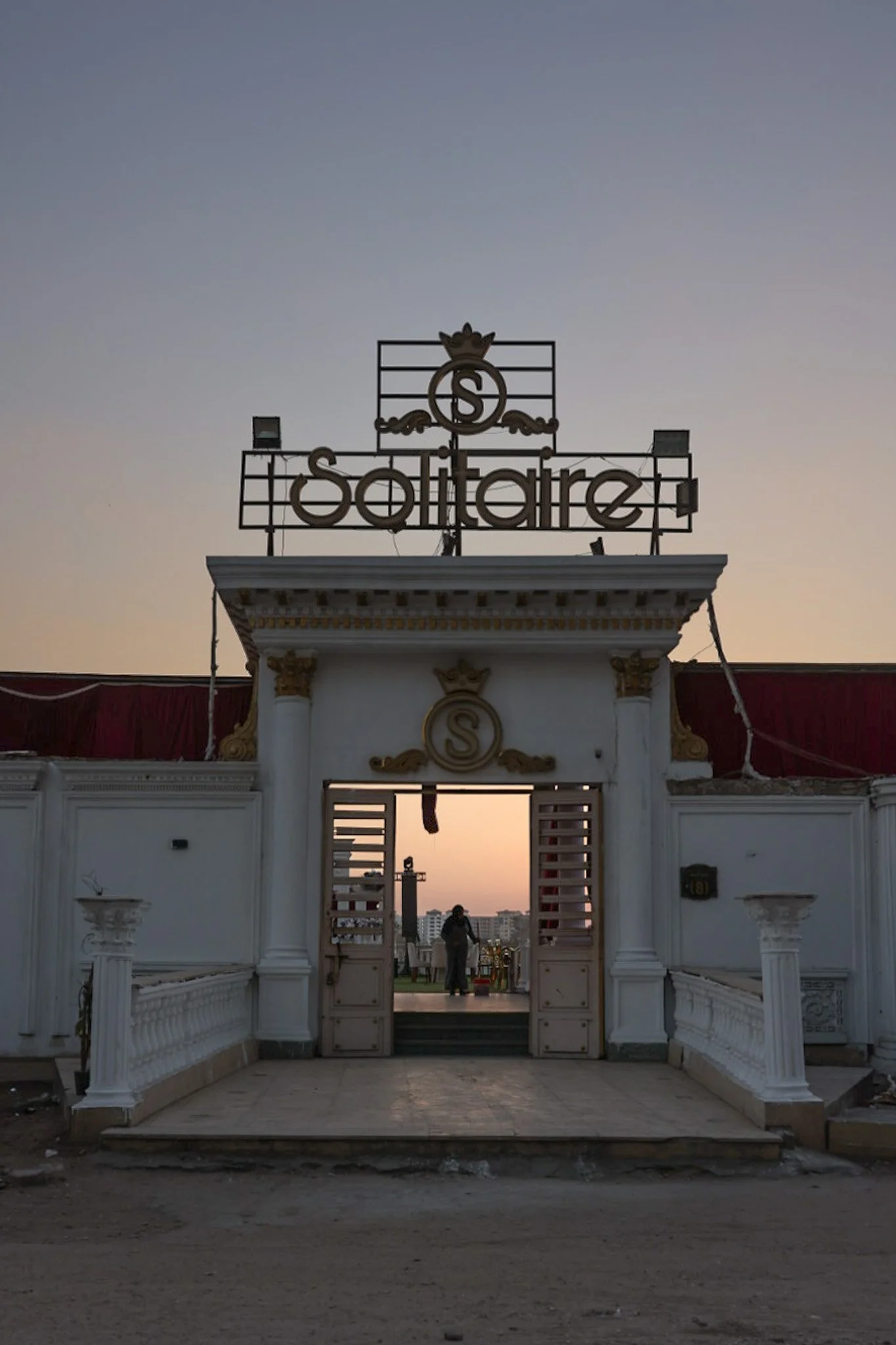 White and gold venue entrance with open doors and sunset sky