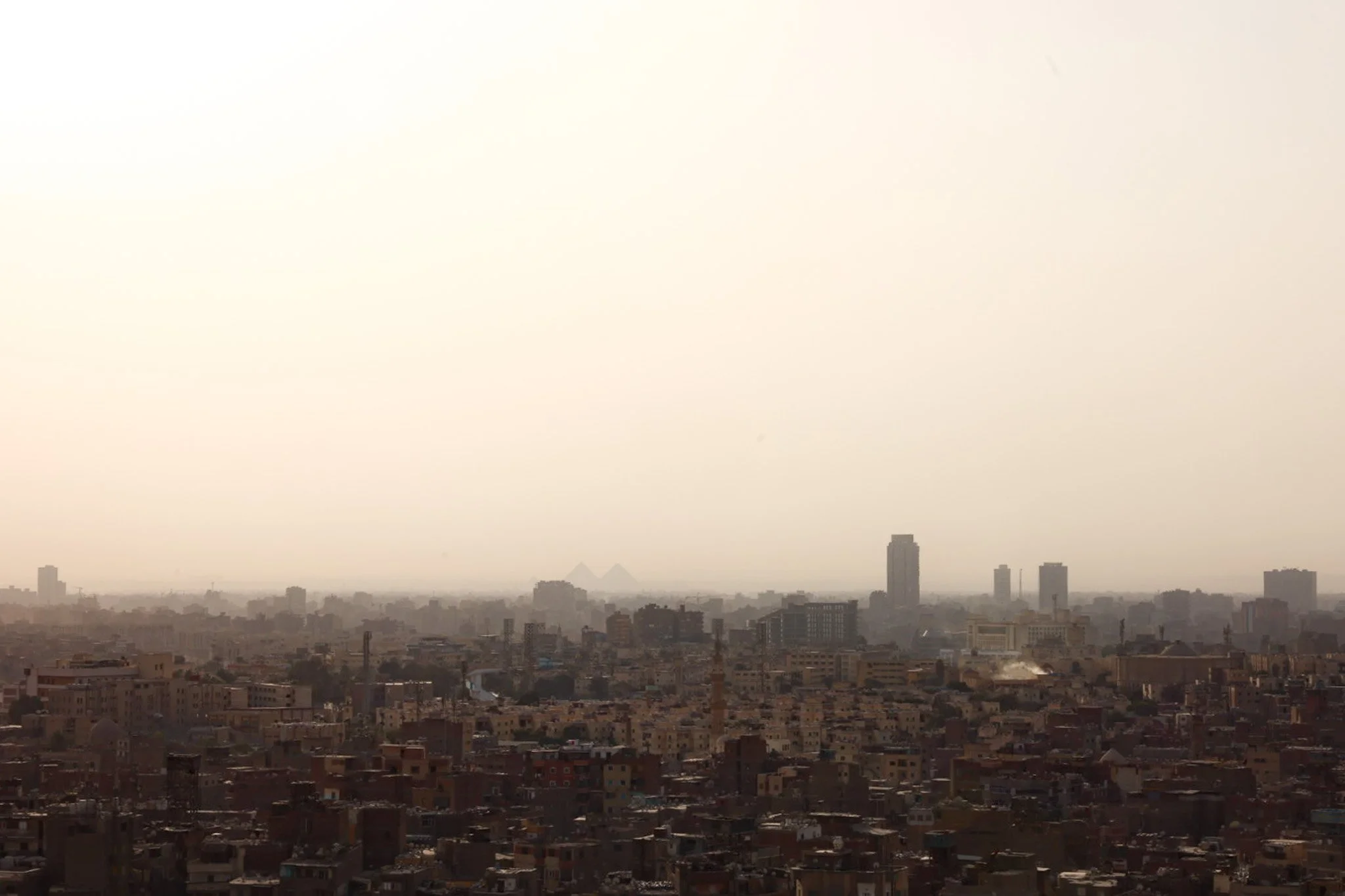 Dense Cairo skyline with pyramids faintly visible through haze