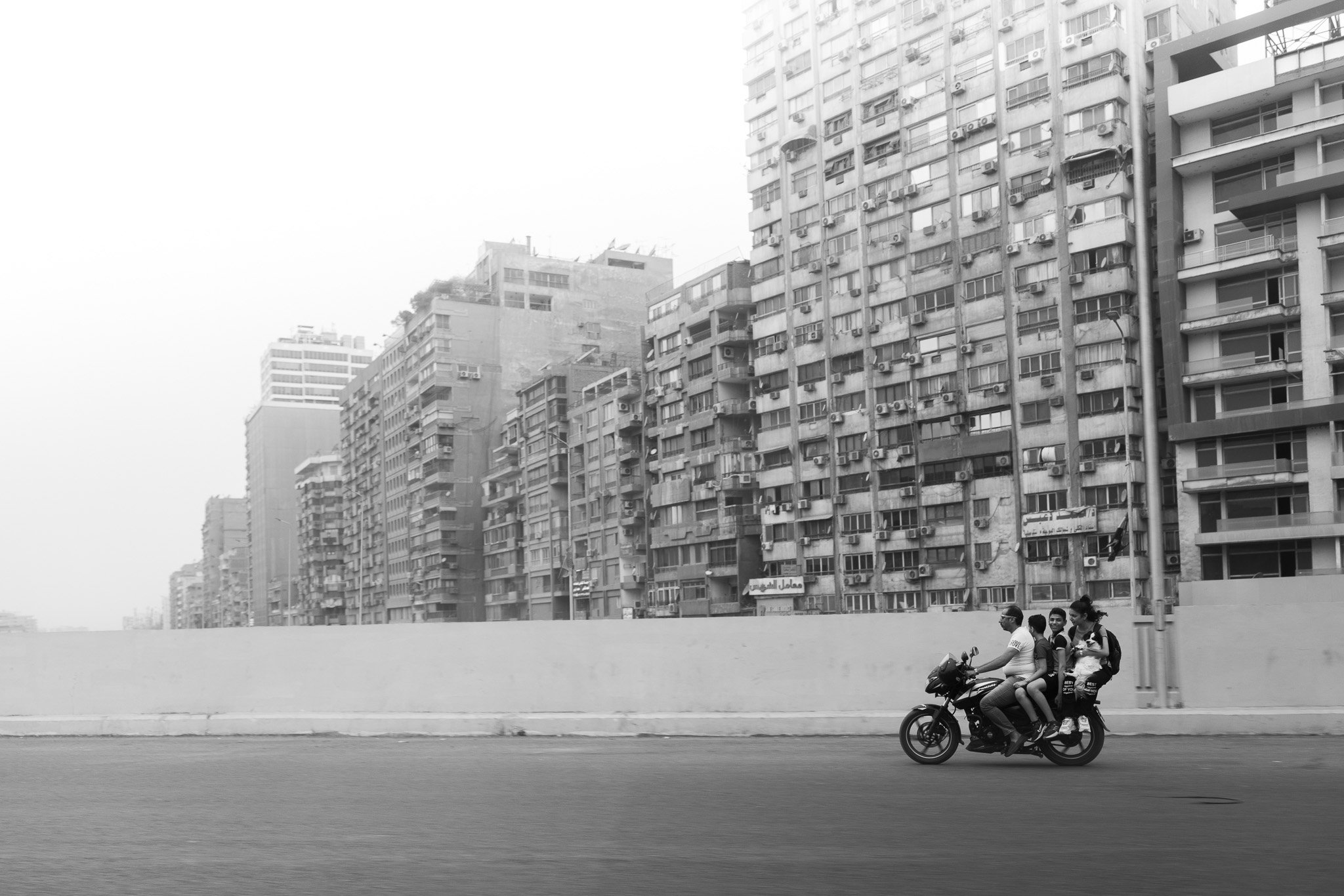 A family with their dog riding motorcycle on empty road with tall apartment blocks behind