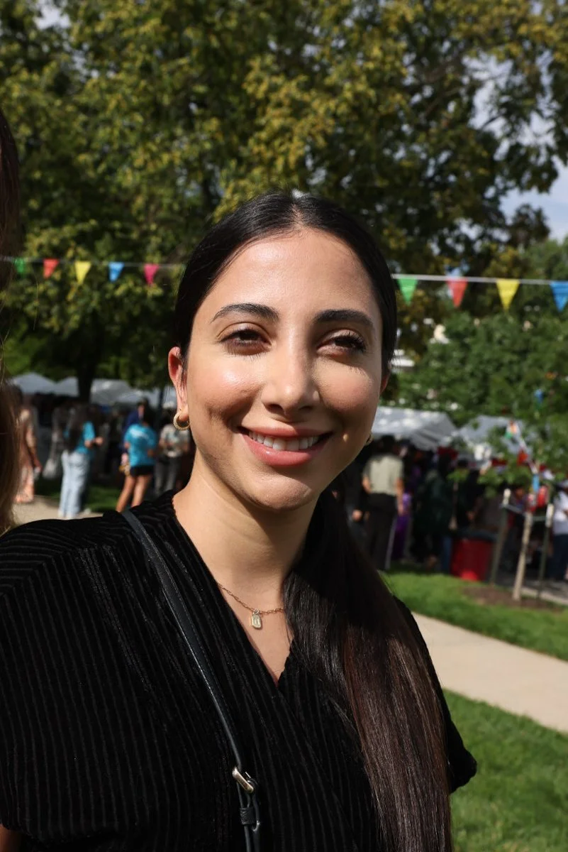 A woman standing outdoors at the Carmel Eid Festival with colorful pennant flags and tents behind her.