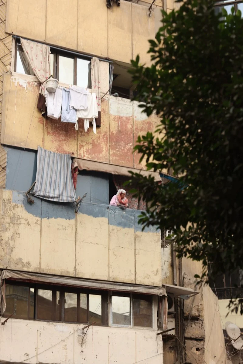 Old apartment façade with peeling paint, laundry, and woman leaning out window