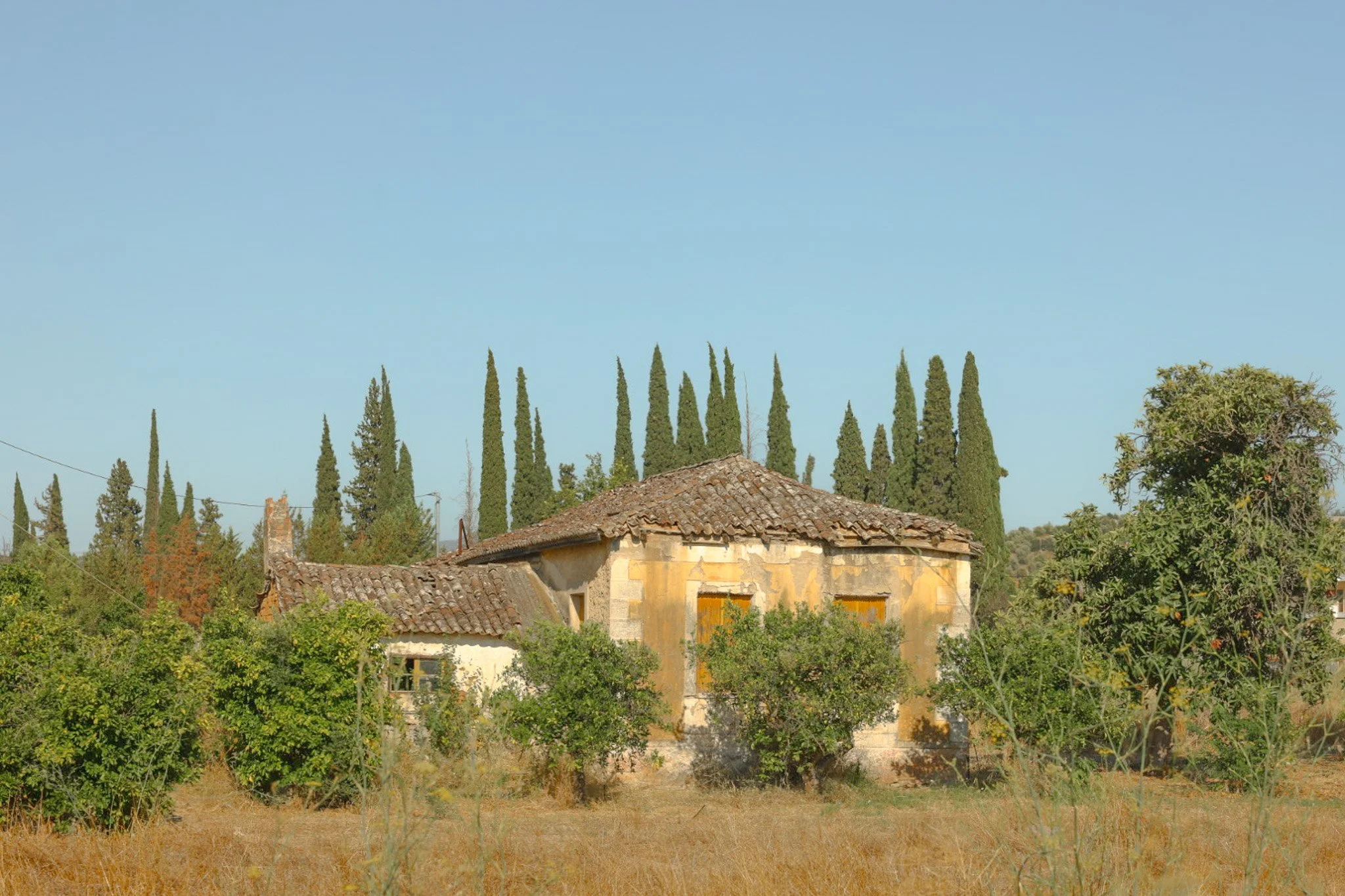 Weathered abandoned farmhouse along the road to Epidaurus near Mycenae, showing cracked plaster, aging stonework, and rural isolation.