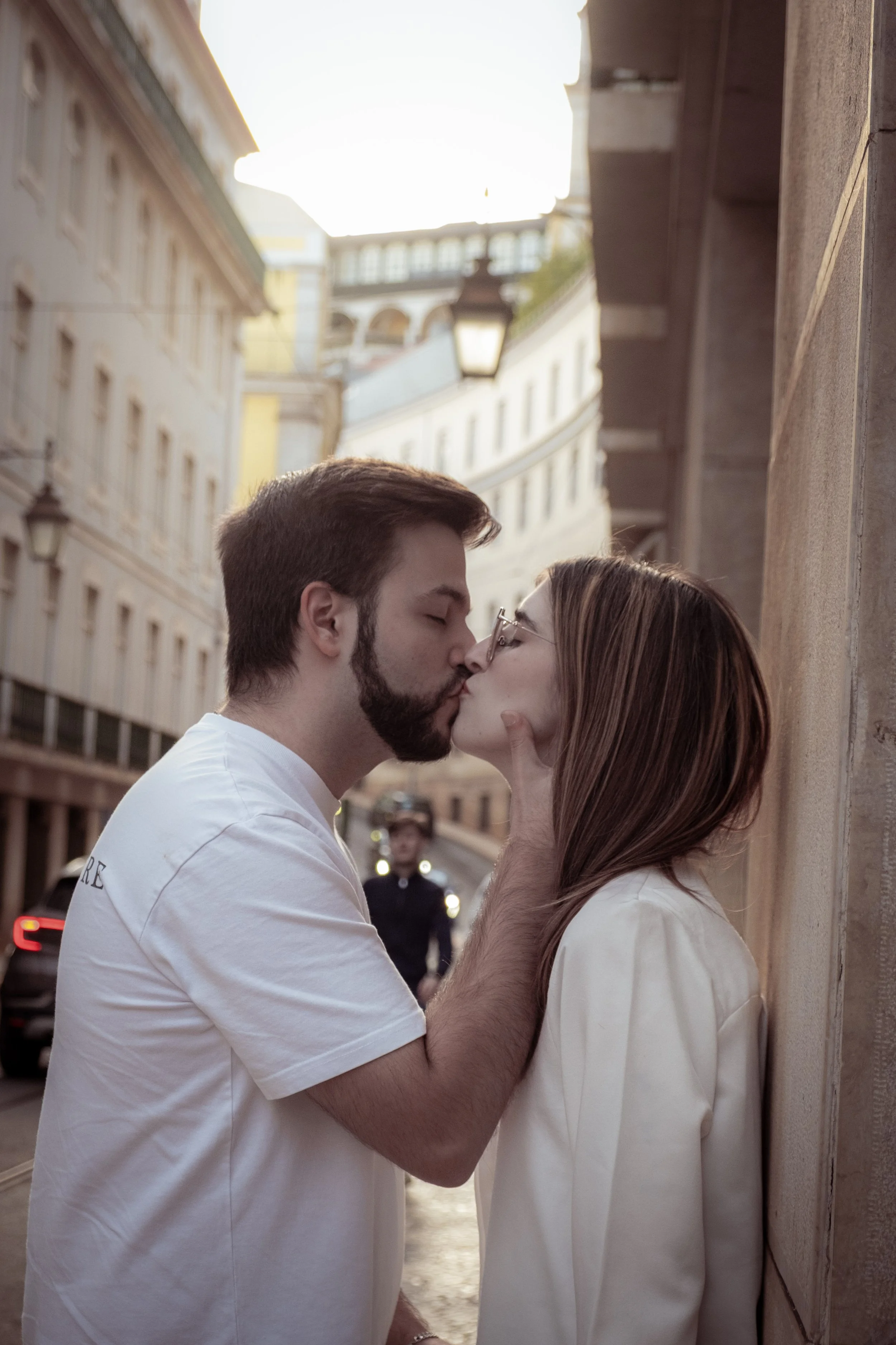 Um casal se beijando na rua ao pôr do sol, com prédios antigos ao fundo.