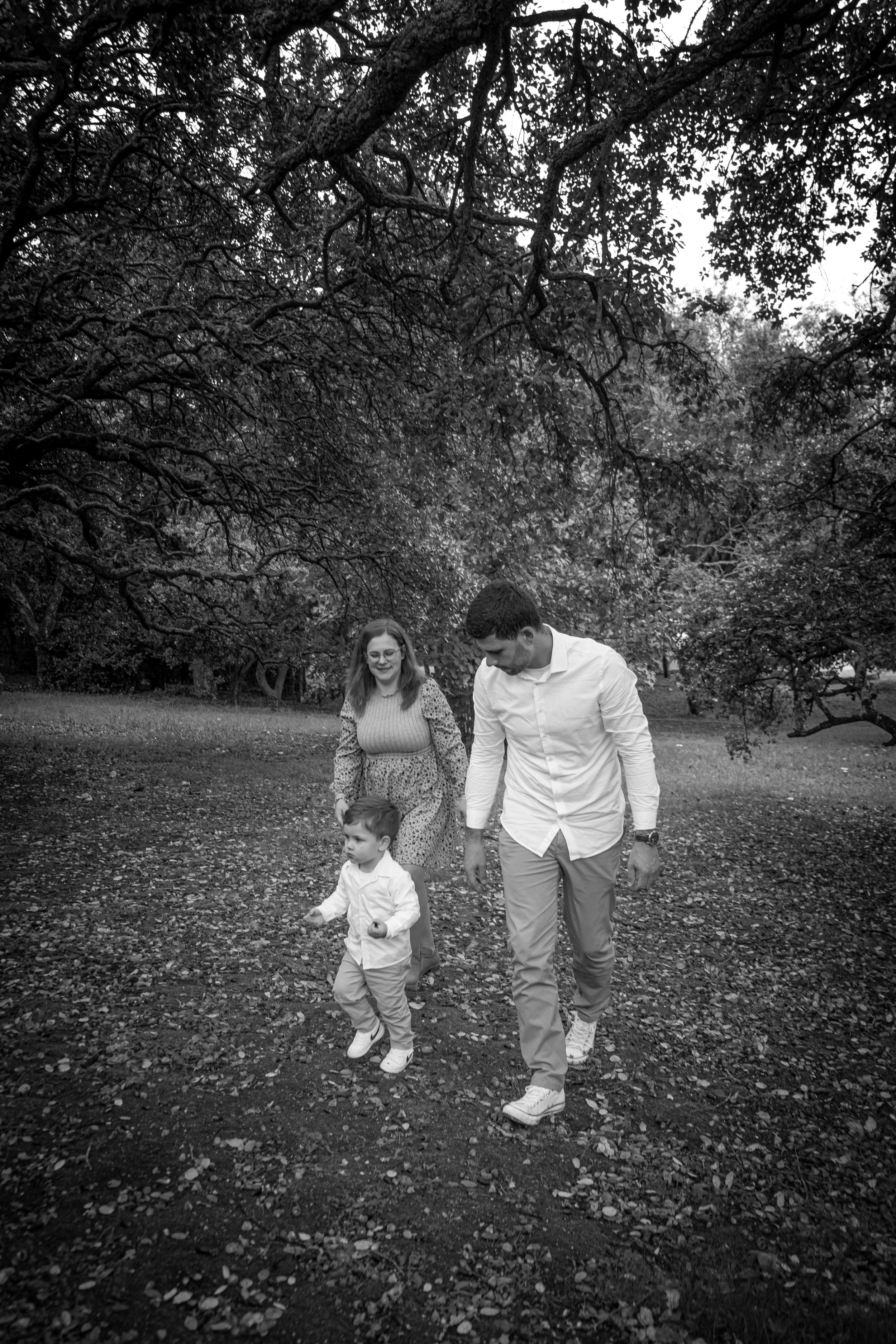 Imagem em preto e branco de uma família caminhando ao ar livre em um parque, com árvores ao fundo.