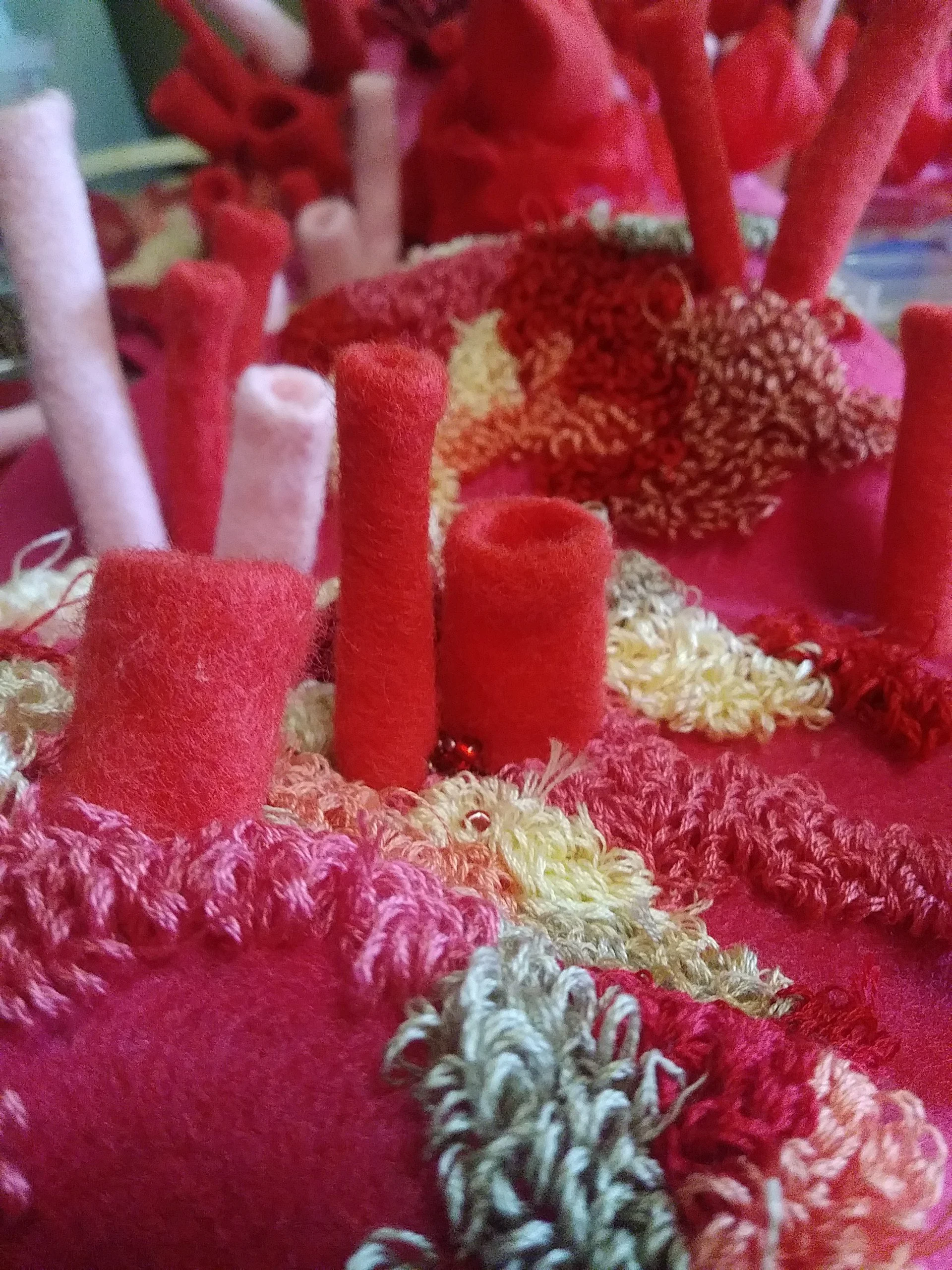 Close-up of various colorful twisted and straight yarns in red, pink, white, and multicolored, arranged on a pink textured surface.