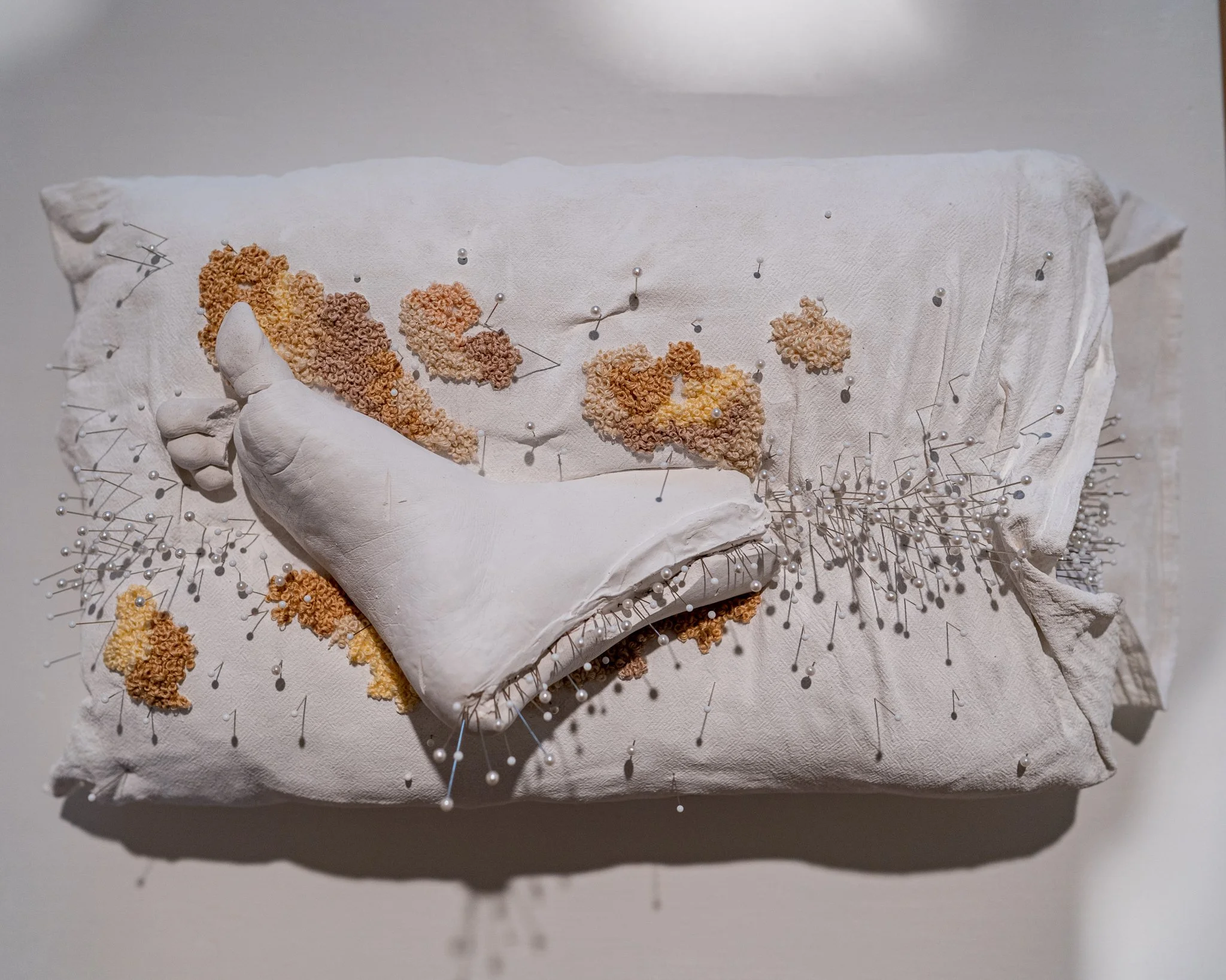 A sculpture of a human foot with three-dimensional star-shaped formations and pearl pins attached to the surface.