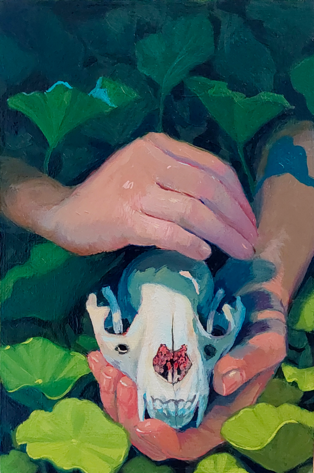 A person holding a small animal skull with a pink nose and eye sockets, surrounded by green leafy plants.