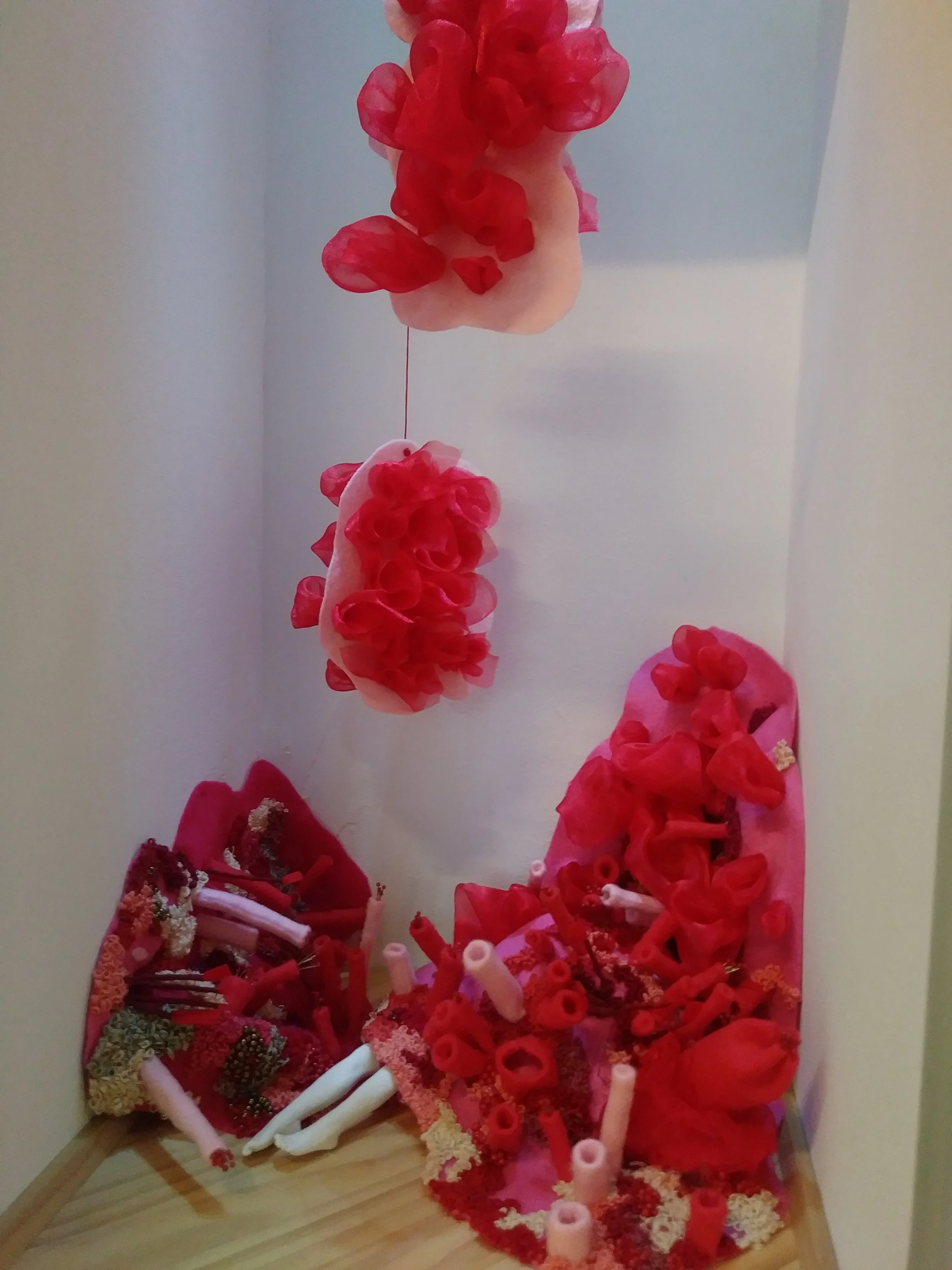 Various red and pink decorative items arranged on a corner shelf, including flowers, textile pieces, and rolled materials.