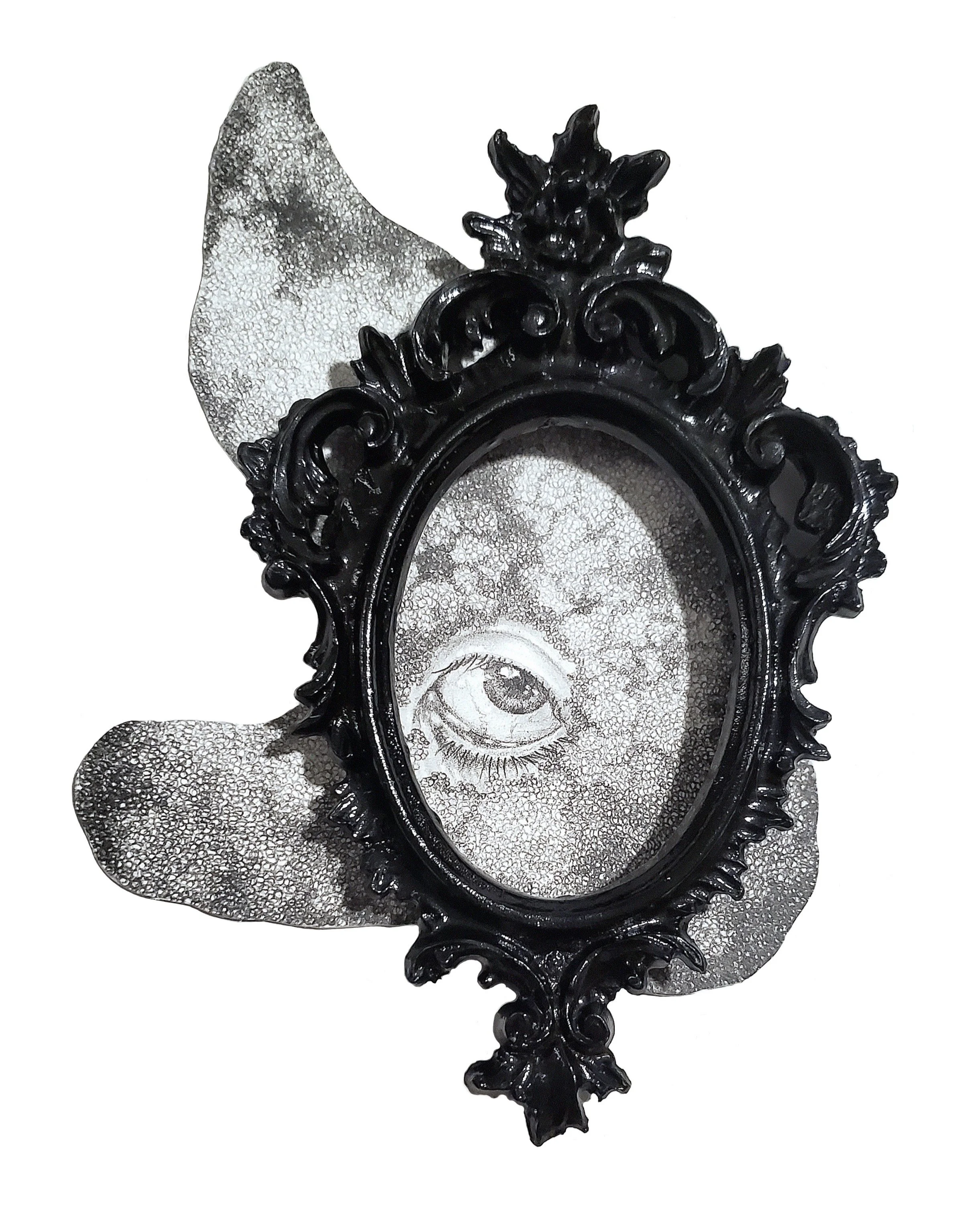 An ornate black picture frame with a vintage eye illustration inside, placed on a textured silver surface with a decorative bow on the left side.