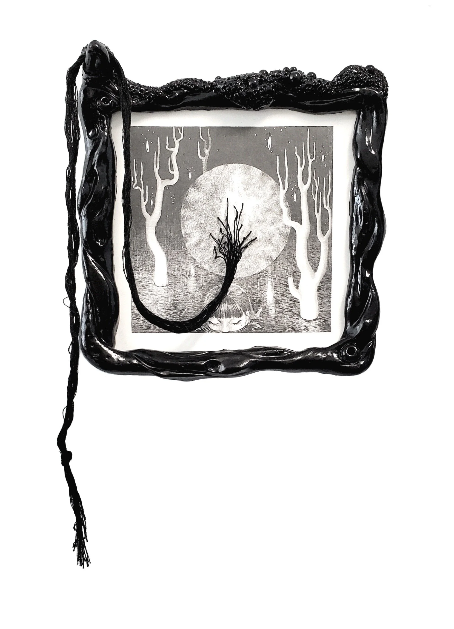 Black ornate picture frame with a black cord hanging over it, positioned in front of a monochrome illustration of a girl with closed eyes, surrounded by trees and a large moon.