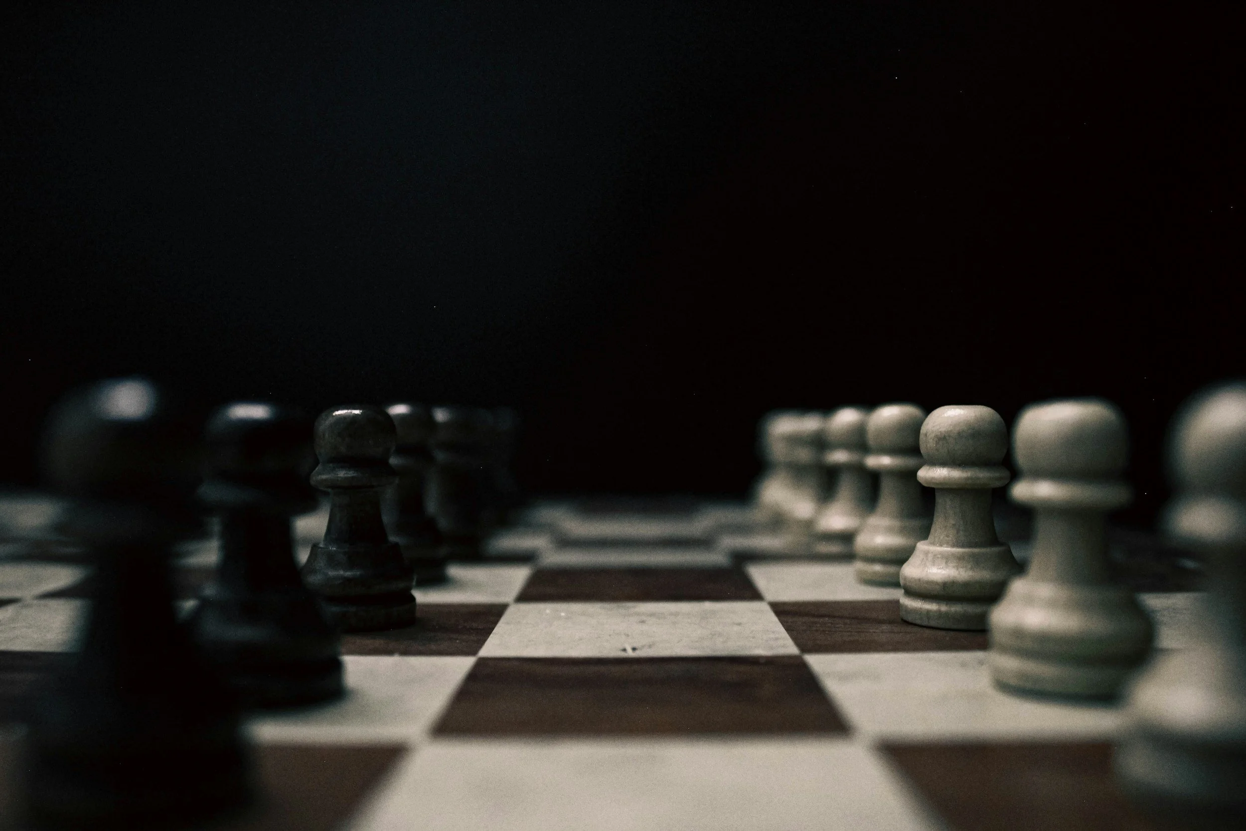 Close-up of a chessboard with black and white chess pieces set up for a game, photographed from low angle.