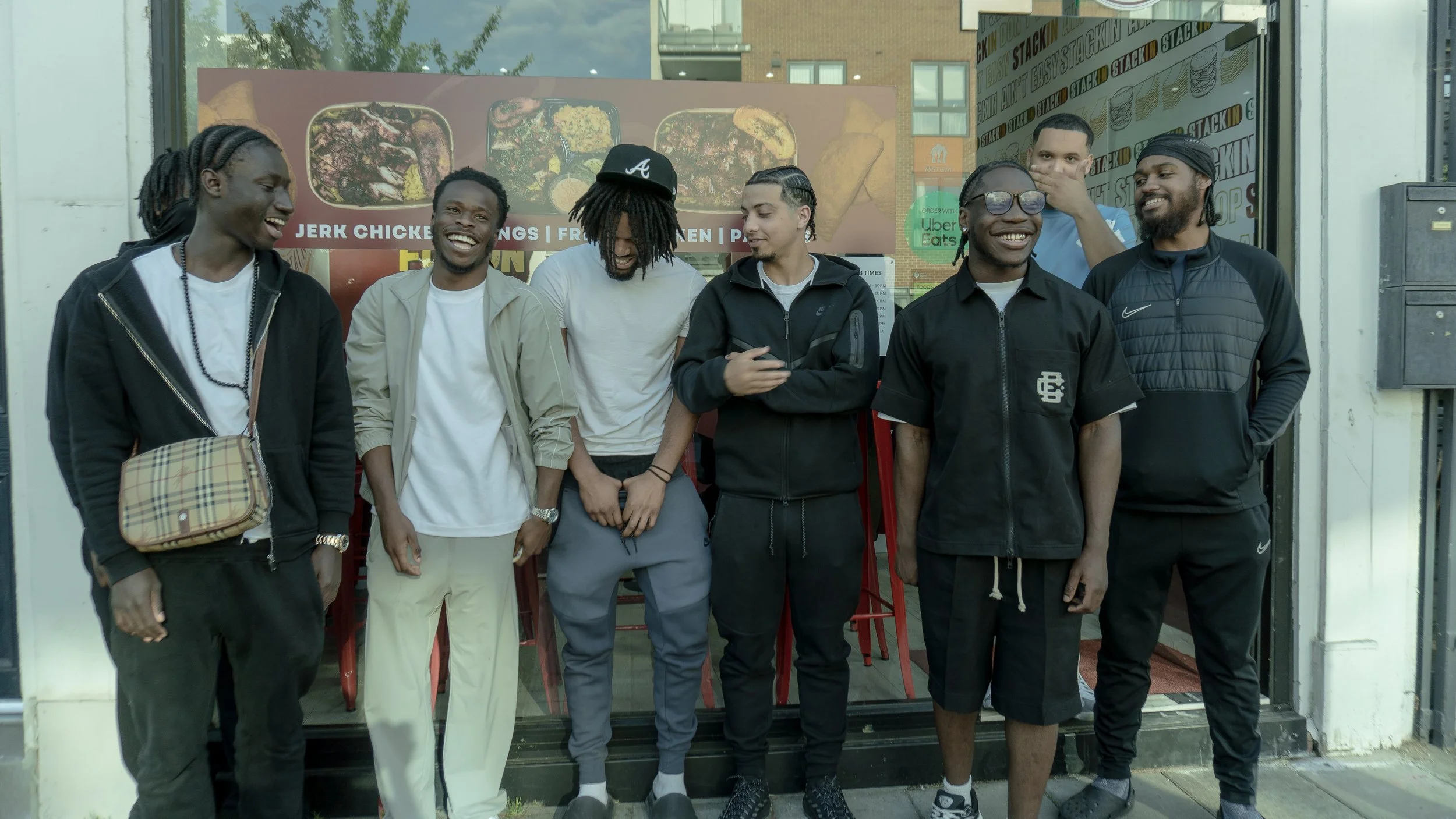 A group of seven young men standing outside a restaurant, laughing and chatting.
