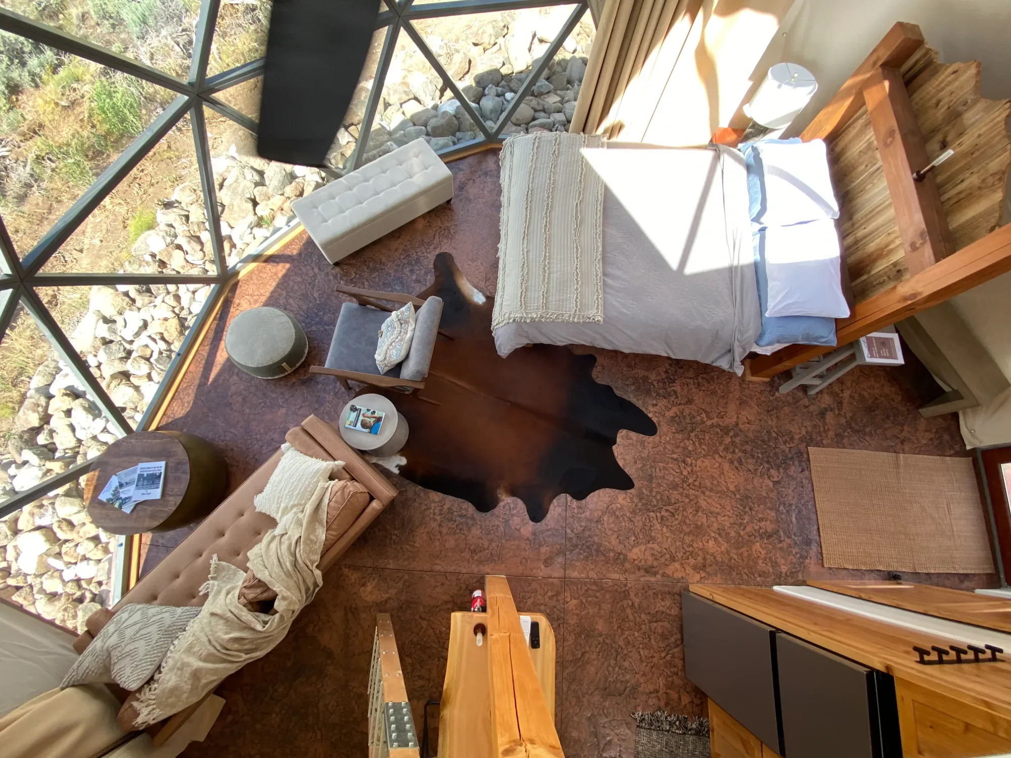 Top-down view of a cozy bedroom with a large bed, large windows, a small table, an armchair, a bench, and a cowhide rug, showcasing a warm and inviting atmosphere.