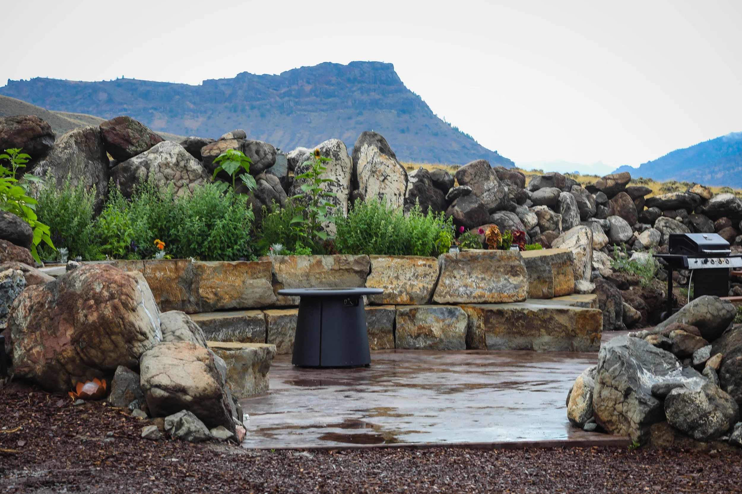 A geodesic dome cabin in a rocky, rural landscape with mountains and a partly cloudy sky in the background. Located in Wapiti Valley, Wyoming at Pure Heart Retreat.
