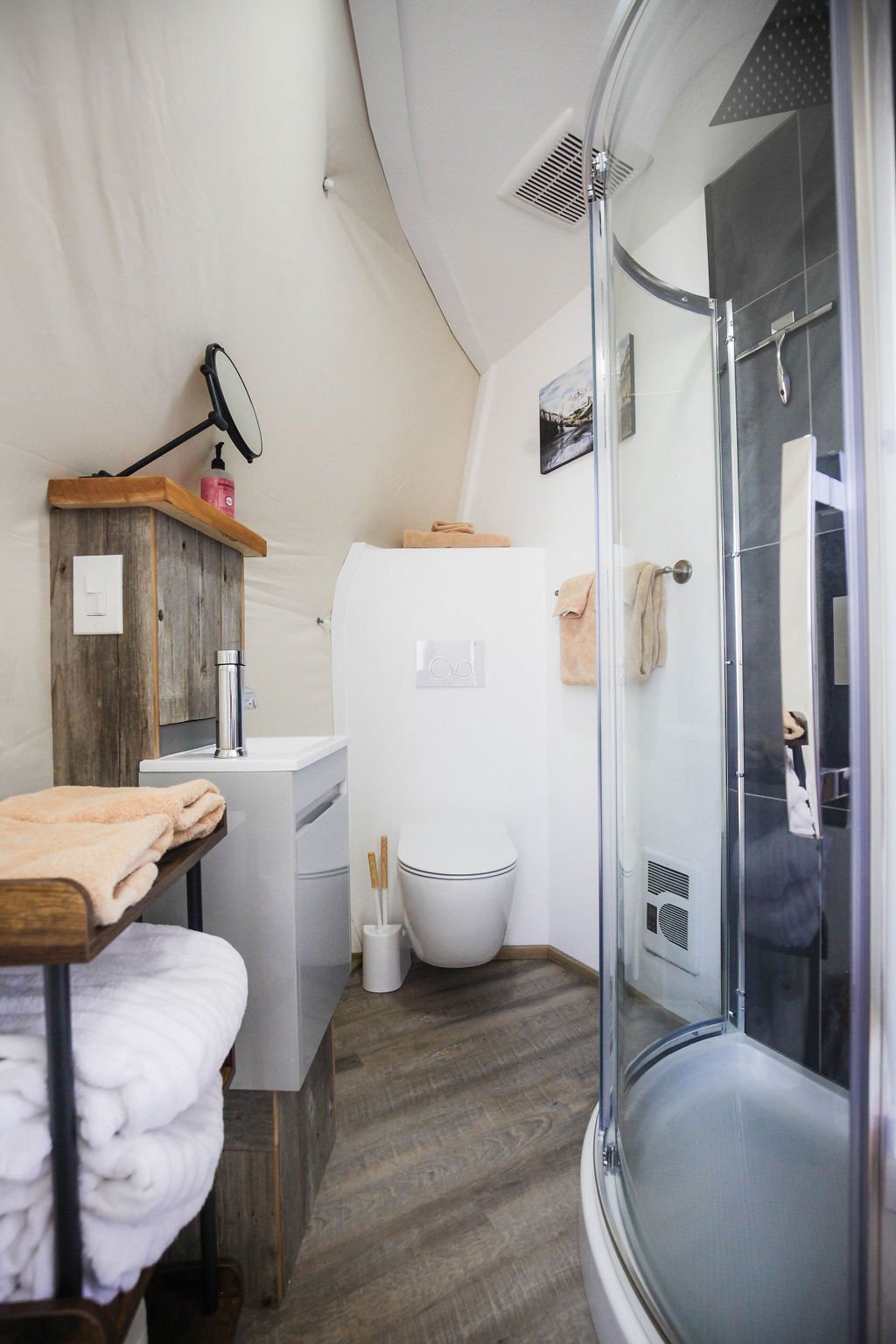Modern bathroom with shower, toilet, small sink, mirror, towels, and wooden accents inside the glamping domes at Pure Heart Retreat in Wapiti Valley, WY.