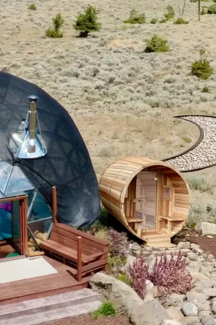 Wooden sauna with open door, situated inside a glass yoga dome with a view of Wapiti Valley, Wyoming outside.