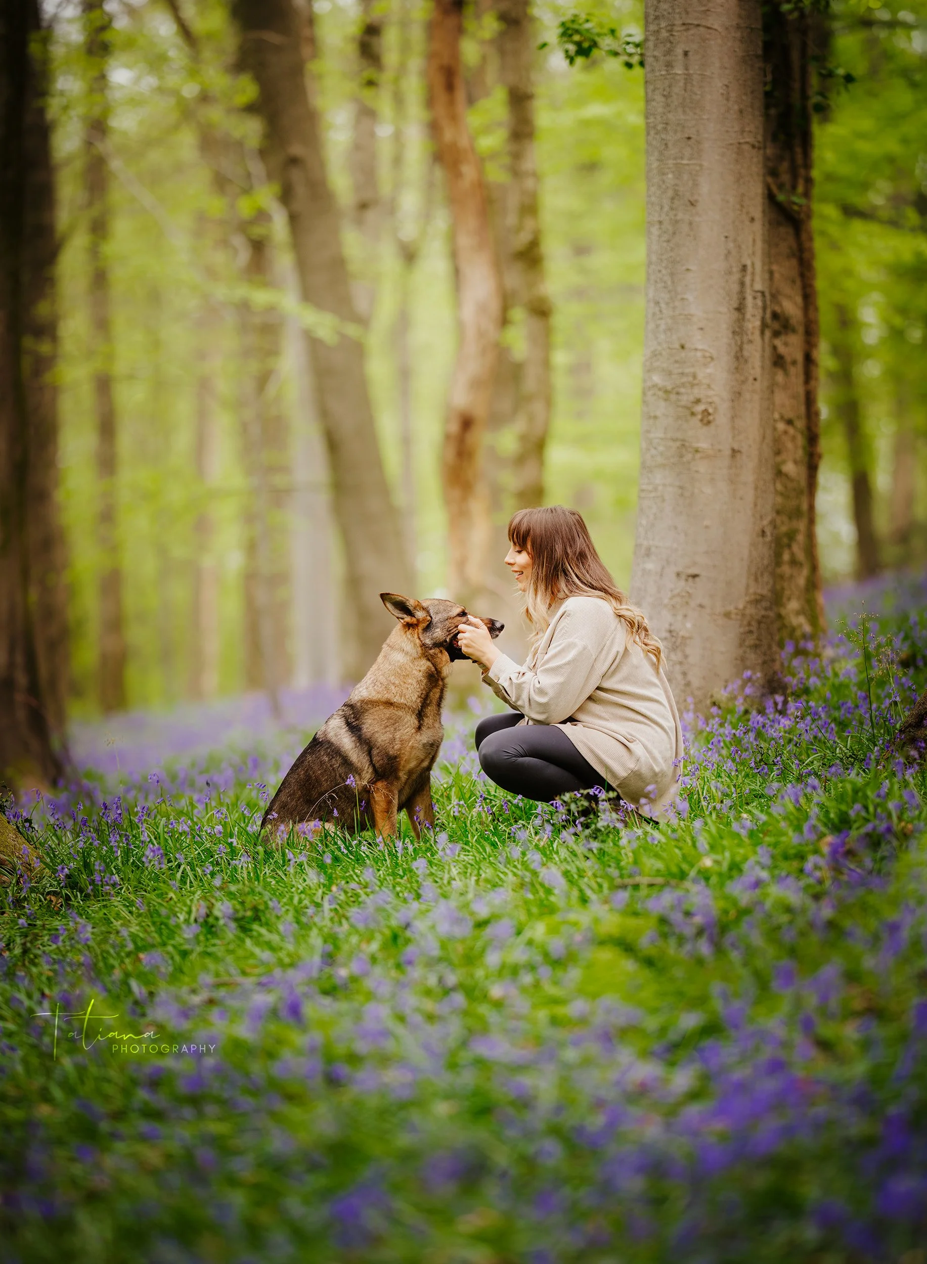 A woman interacting with a dog in a forest surrounded by purple flowers.
