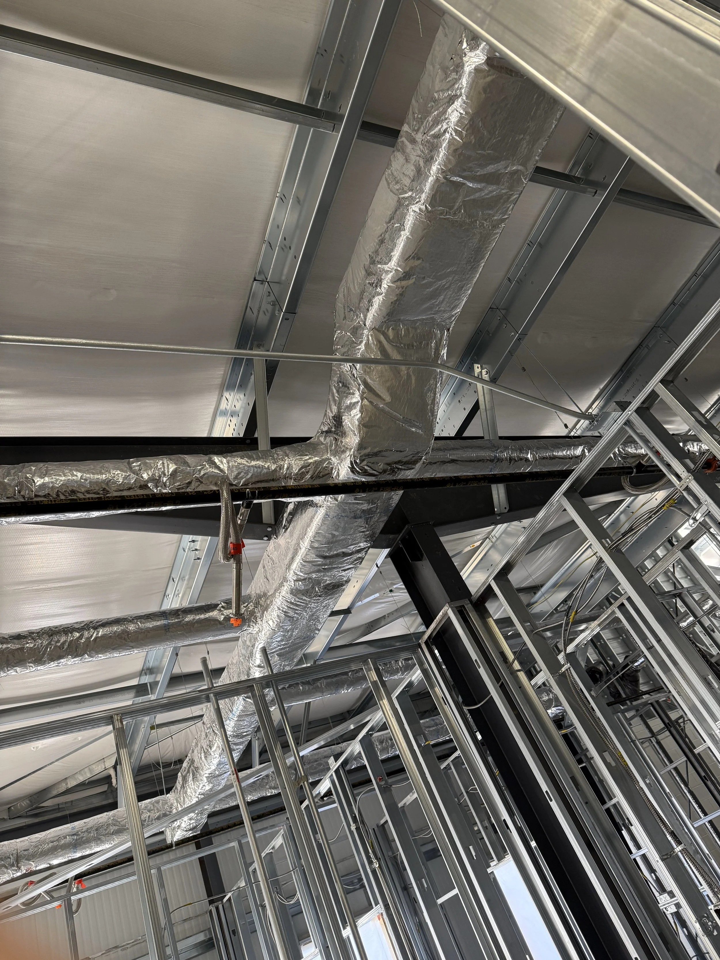 Construction site ceiling with metal framework, ductwork, and electrical wiring.
