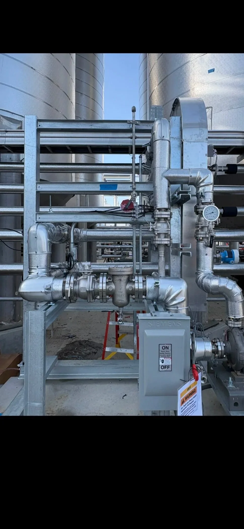 Industrial piping system with metal pipes, valves, and a control box at a construction site.