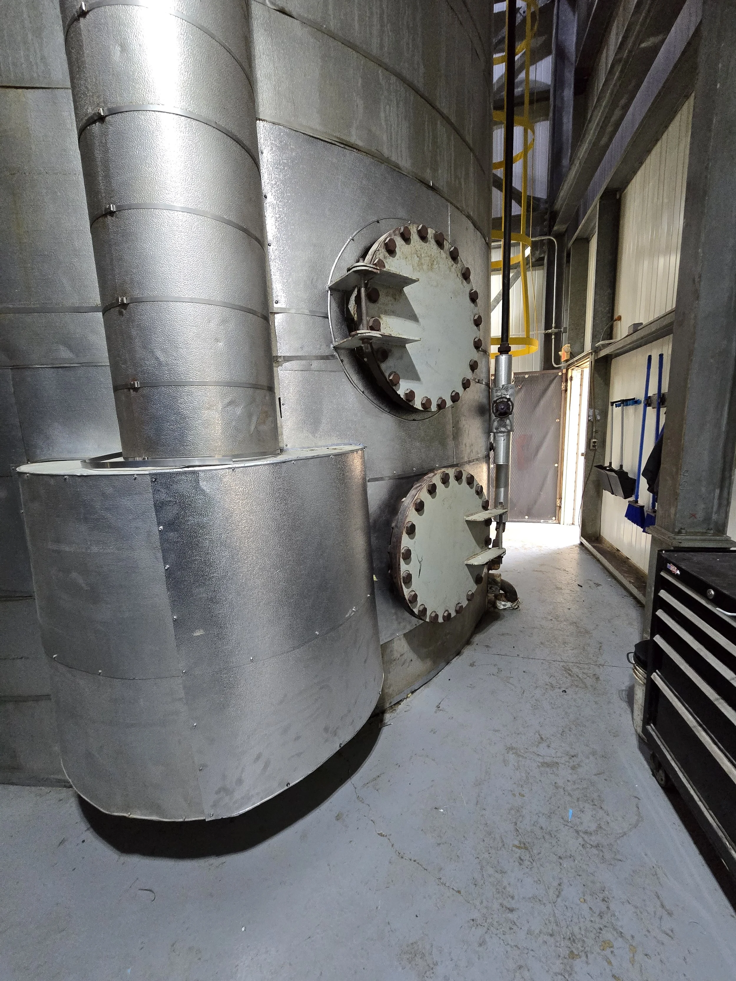 Industrial ductwork with large circular access panels and a toolbox against a wall in a workshop.