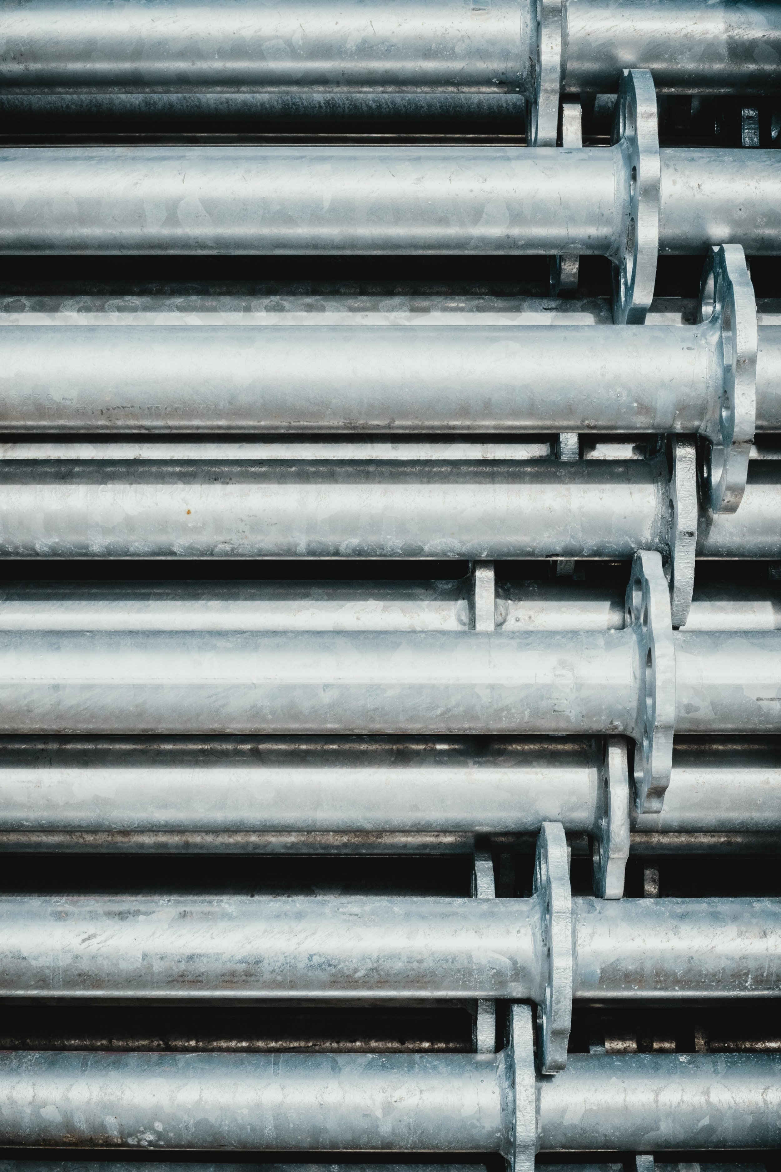 Stacked metal pipes with flanges, silver in color, arranged horizontally.