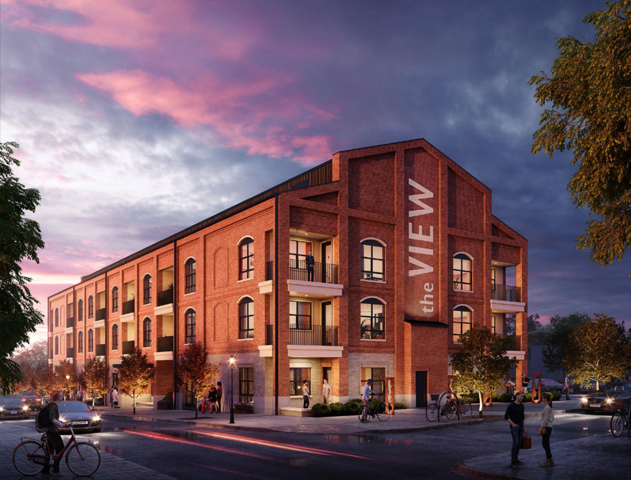 A newly constructed mixed-use building with retail and residential units, featuring brick facade and large arched windows, situated in an urban area at dusk with people walking and biking, and cars on the street.