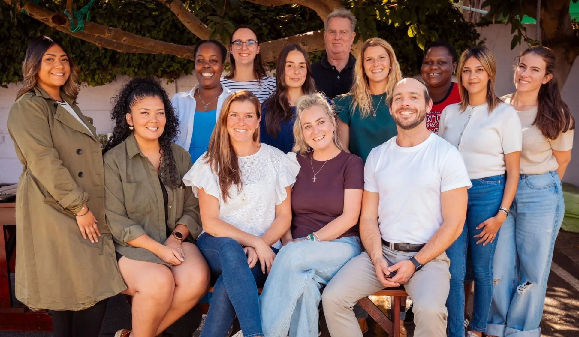 A diverse group of people posing outdoors in front of trees, smiling and looking at the camera.