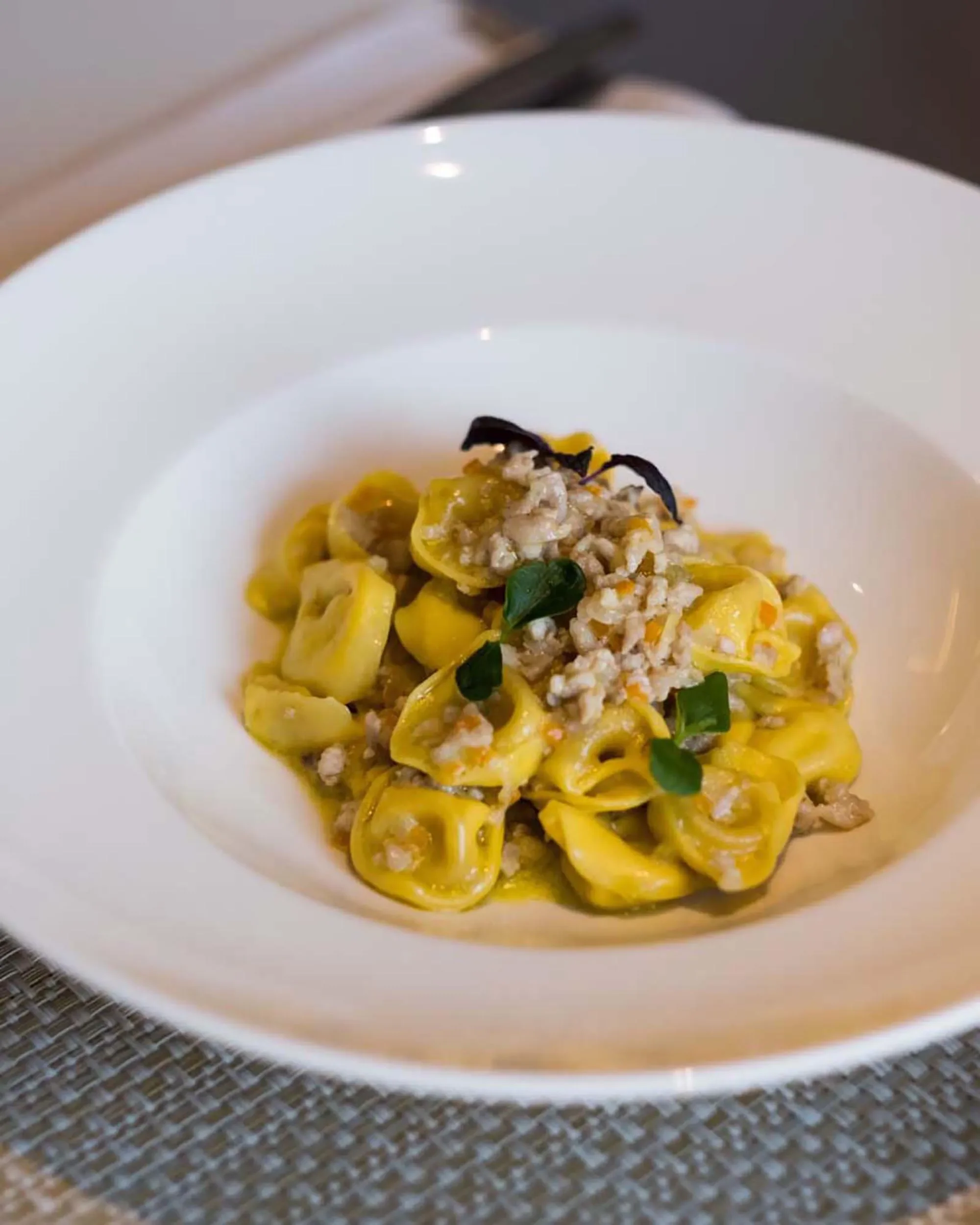 Piatto di pasta ripiena con ripieno di carne, guarnito con erbe fresche e crocchette di carne sopra, in una ciotola bianca.