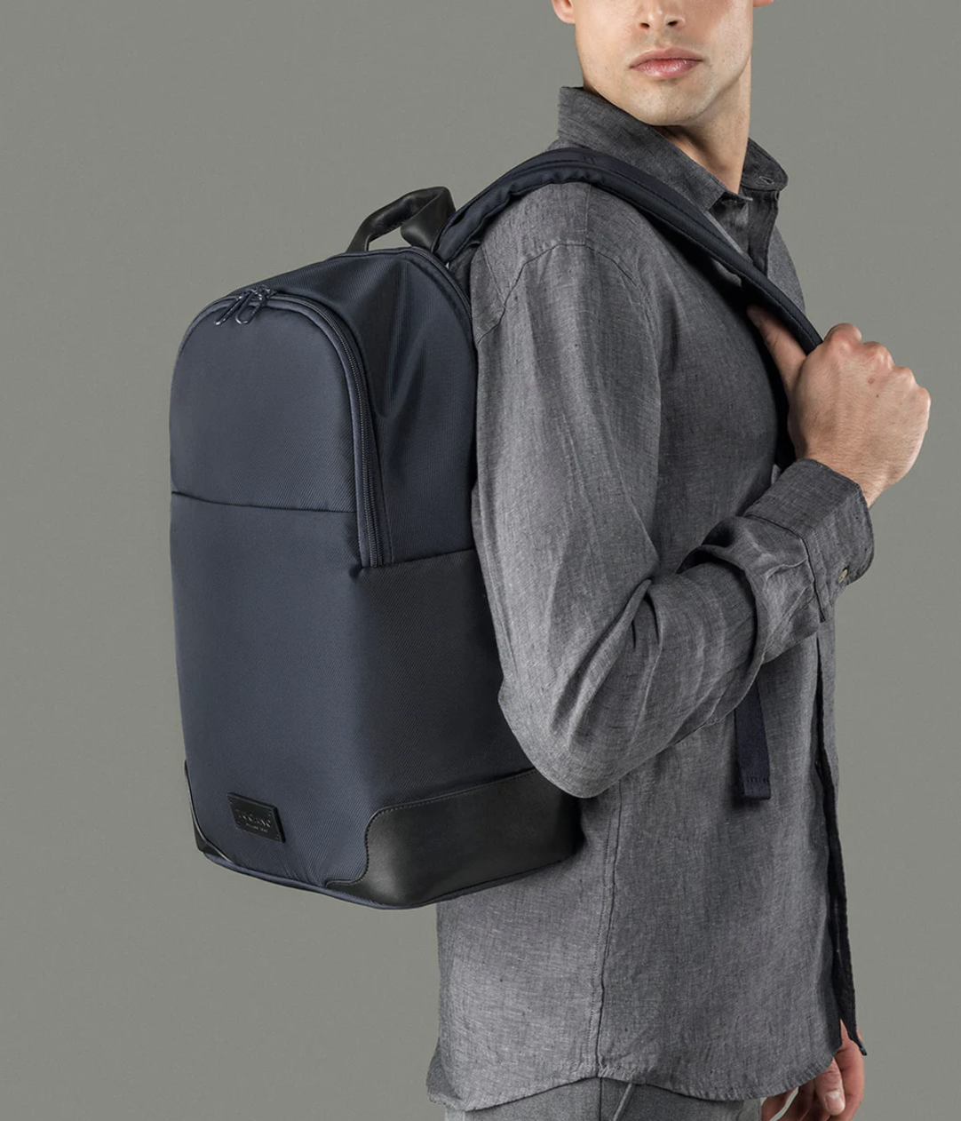 Uomo che indossa una camicia grigia con uno zaino blu sulle spalle.