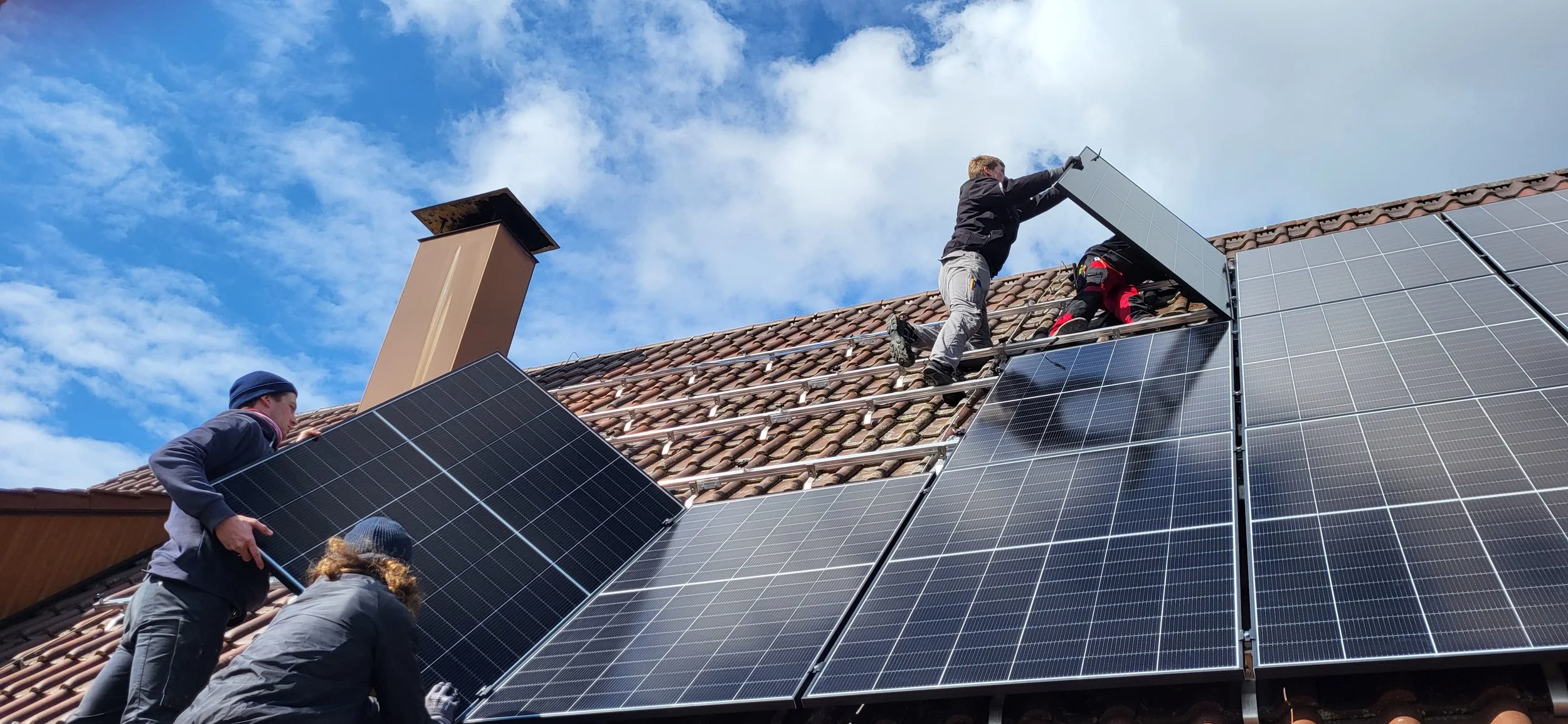 Dachdecker installiert Solarmodule auf einem geneigten Dach bei sonnigem Himmel.
