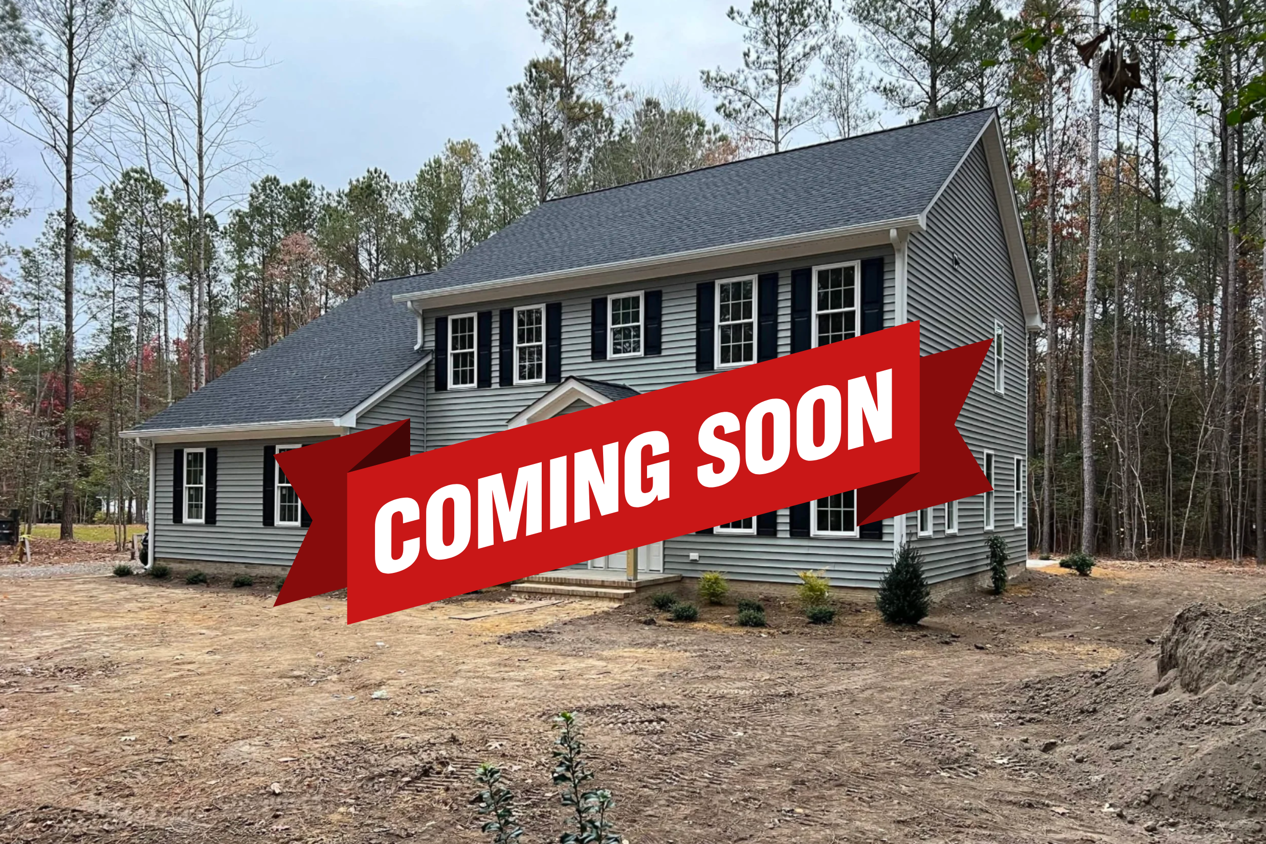 Newly built two-story house with gray siding and black shutters, surrounded by a cleared yard and forested area in the background.