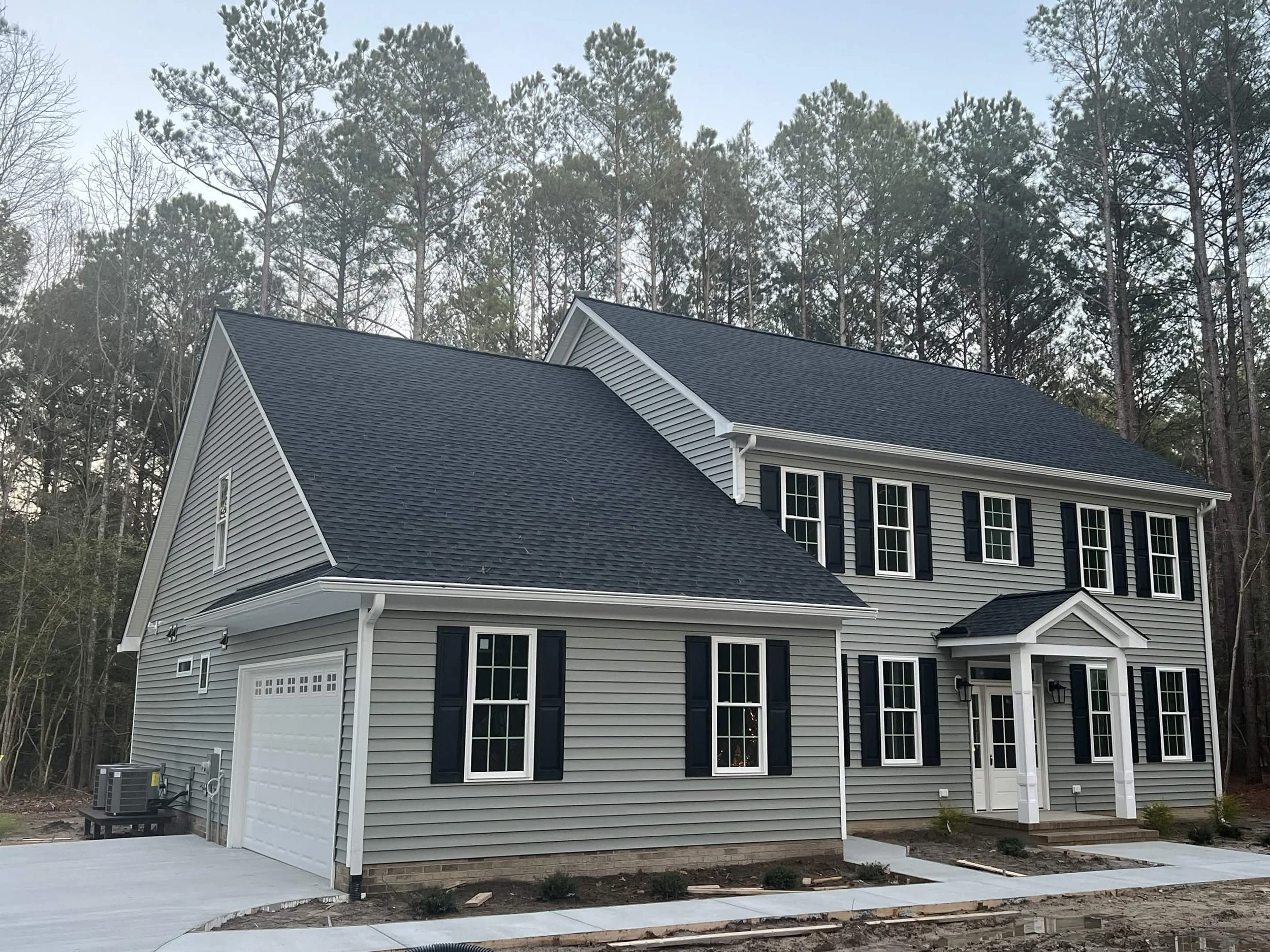 New two-story house with gray siding, black shutters, and white trim, located near a wooded area.