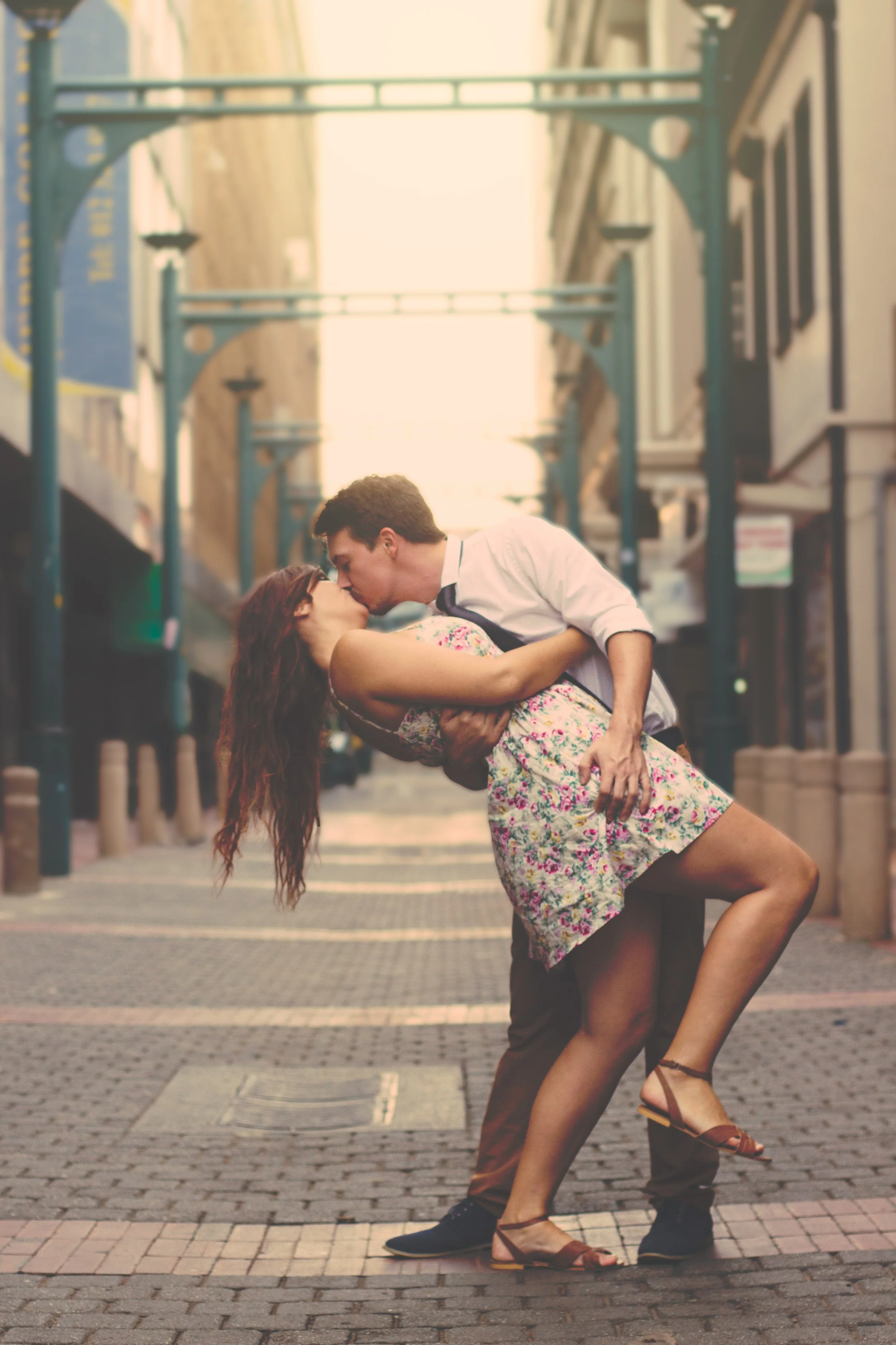 A couple kissing, with the man dipping the woman, in a city street during sunset.