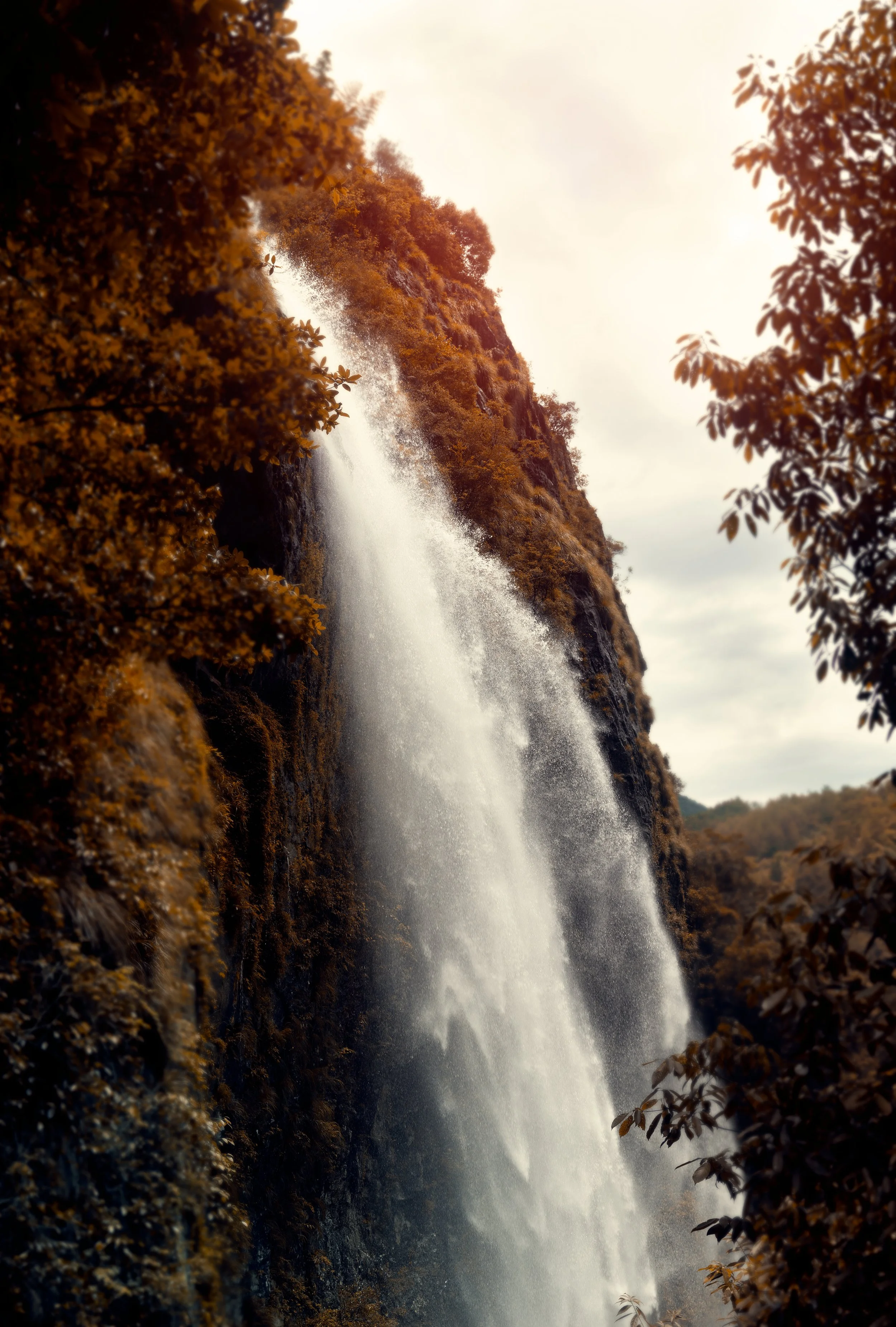 Waterfall flowing down a rocky cliff surrounded by trees with autumn-colored leaves.