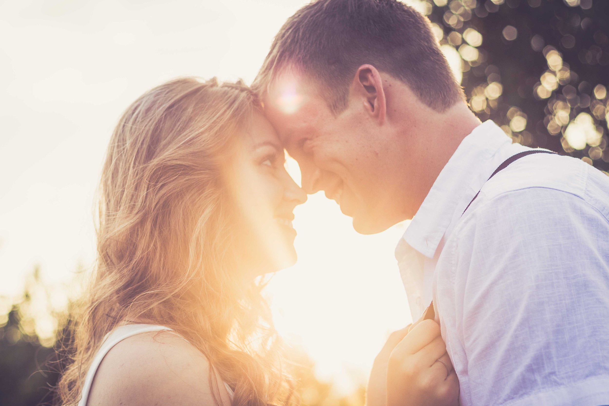 A couple with their foreheads touching, smiling in warm sunlight outdoors.