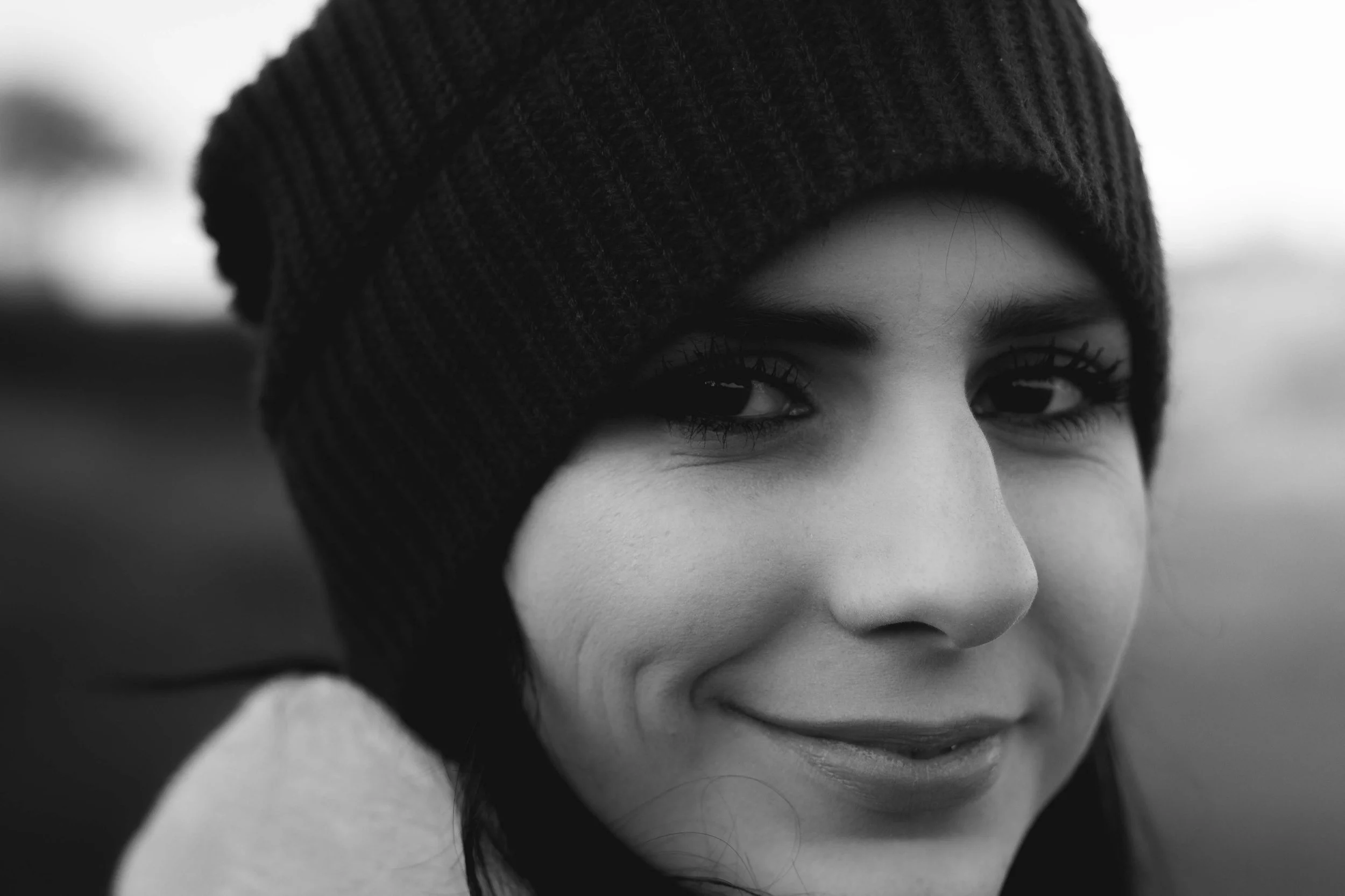 Close-up of a young woman with dark hair, wearing a knit cap, smiling softly, in black and white.