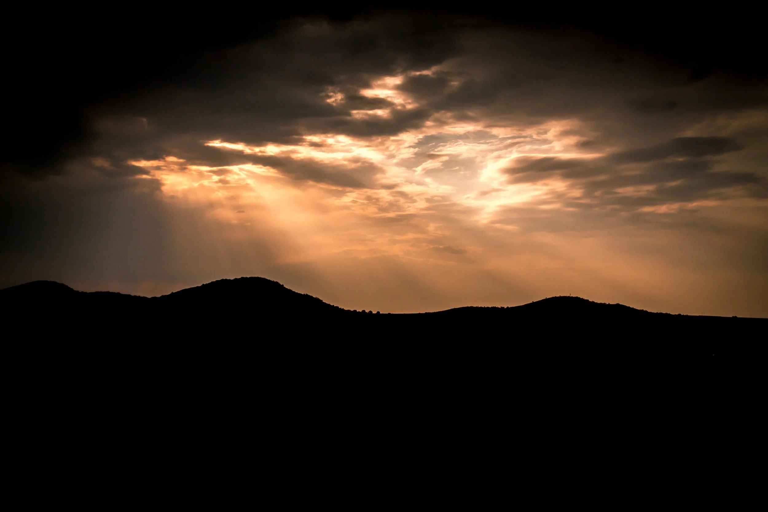Sunset over silhouette mountains with rays of light breaking through clouds.