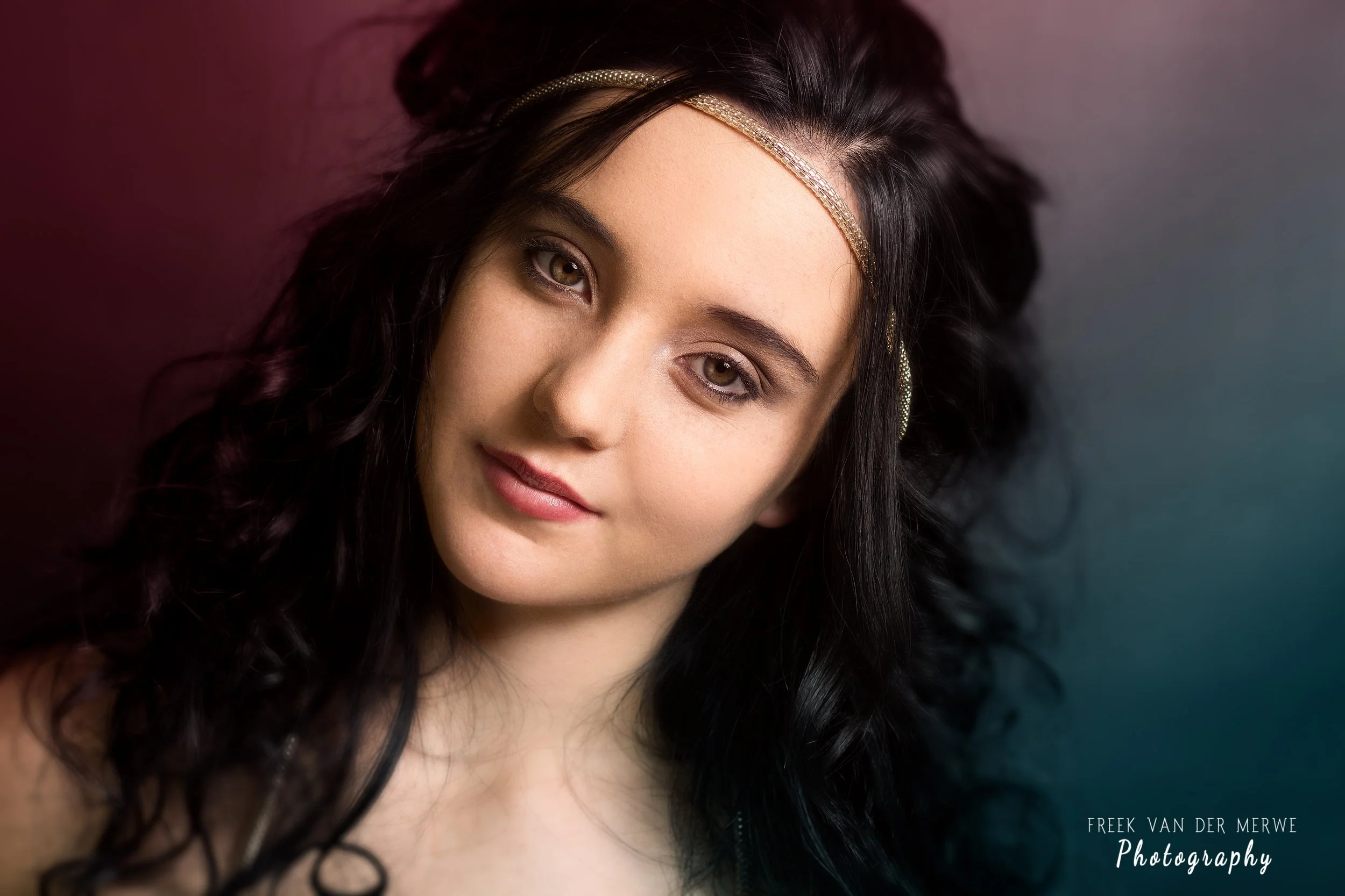A young woman with long black curly hair wearing a gold headband, looking at the camera with a slight smile, against a blurred gradient background.