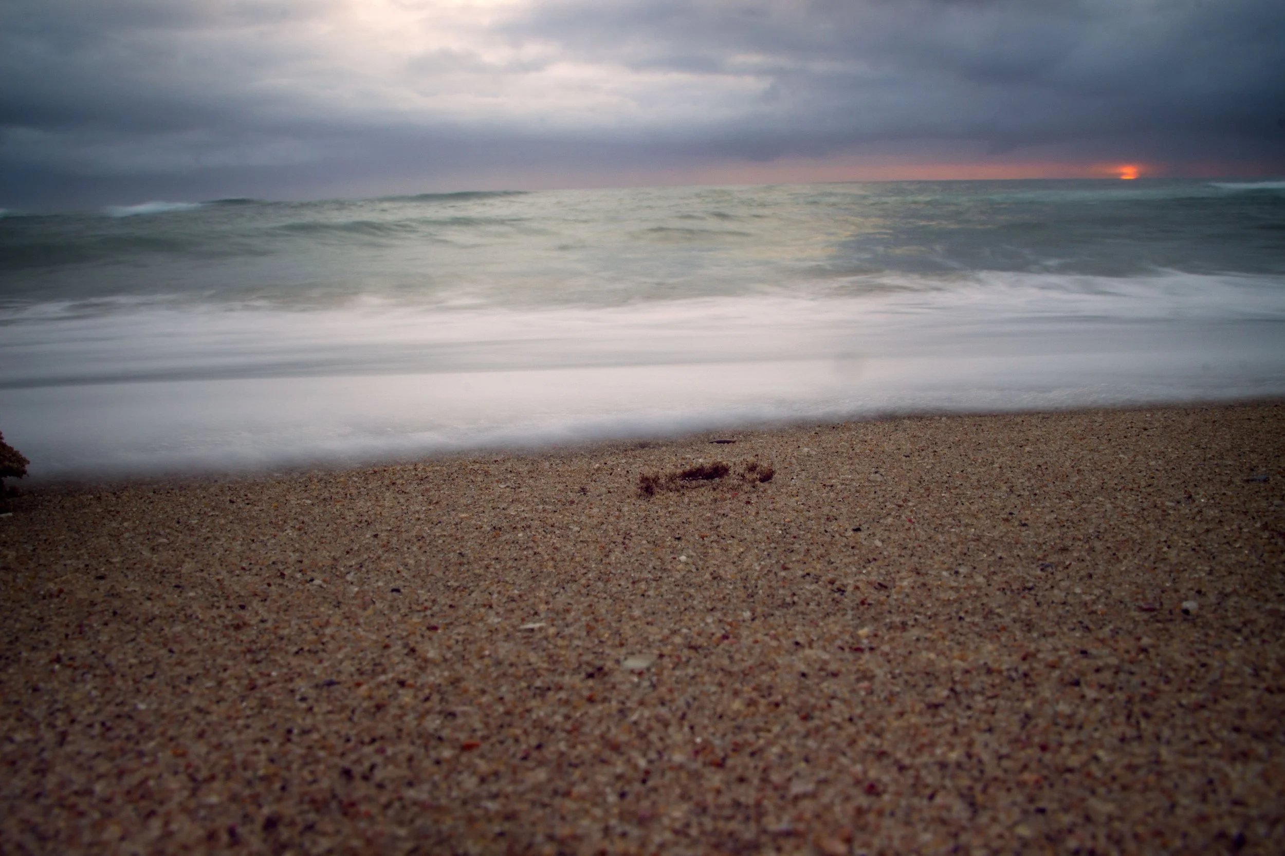 A sandy beach with ocean waves and a cloudy sky at sunset.