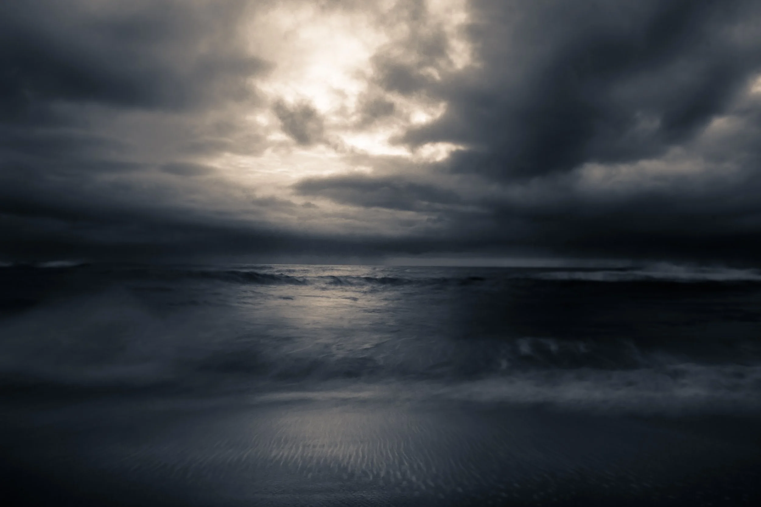 Dark, cloudy sky over the ocean with waves crashing onto the shore.