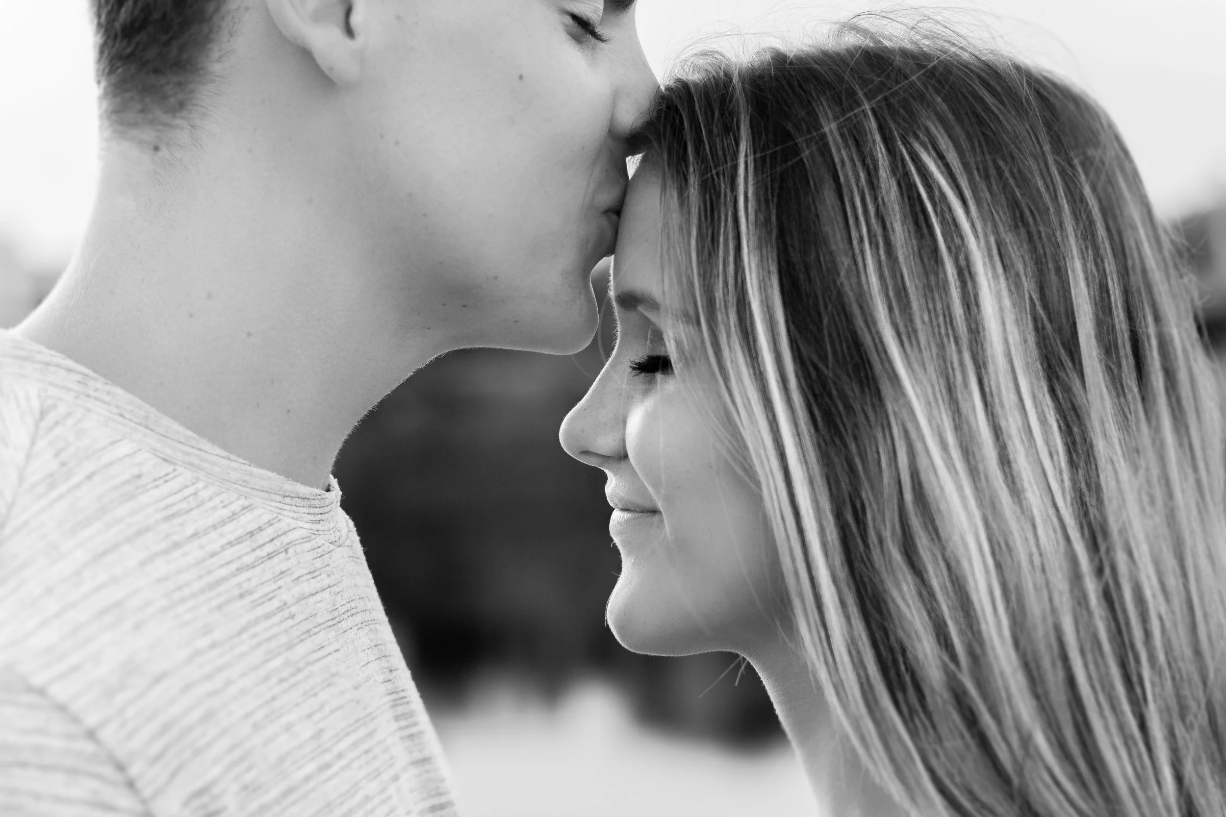 A black and white photo of a young couple with their foreheads touching, eyes closed, smiling gently.